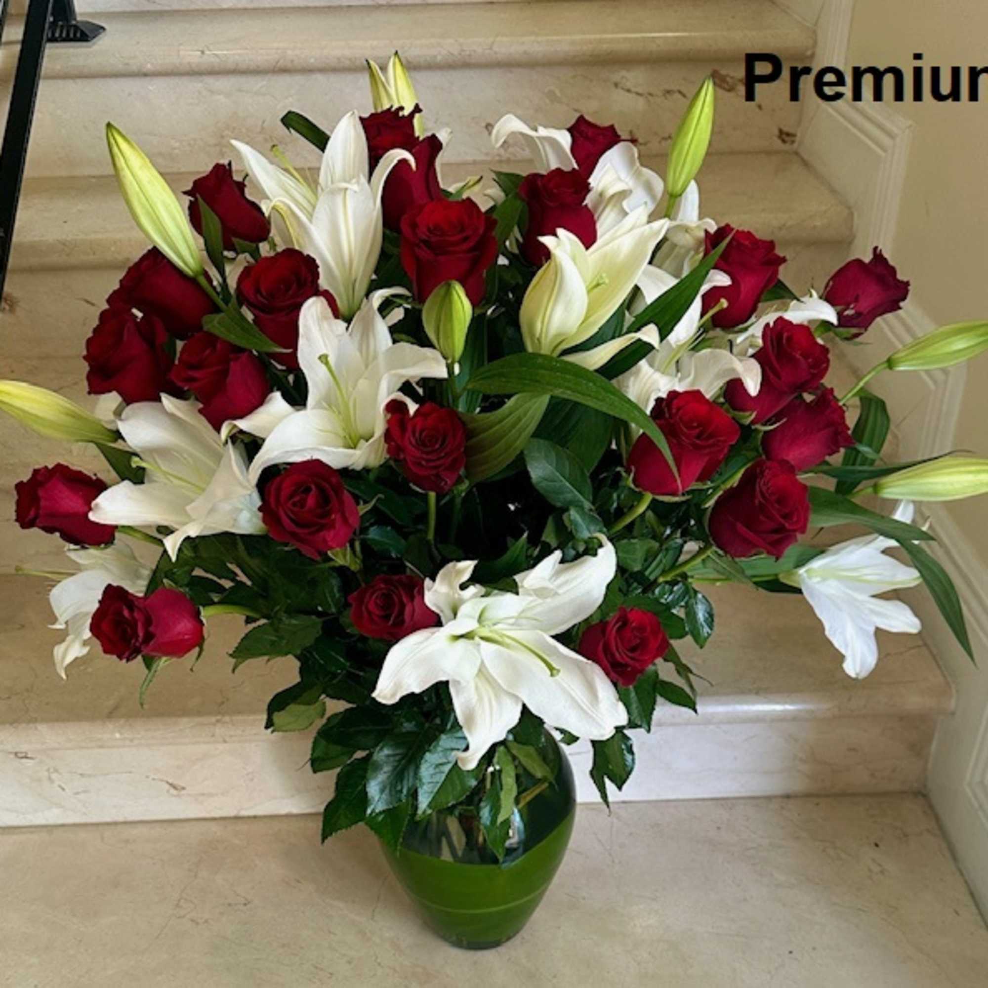 Large arrangement of red roses and white lilies in a green glass vase on stone steps