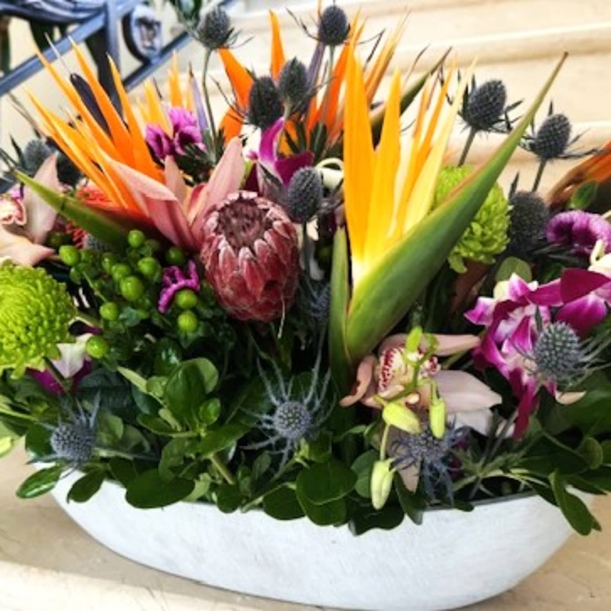 Tropical floral arrangement in a white bowl vase with orange and purple blooms