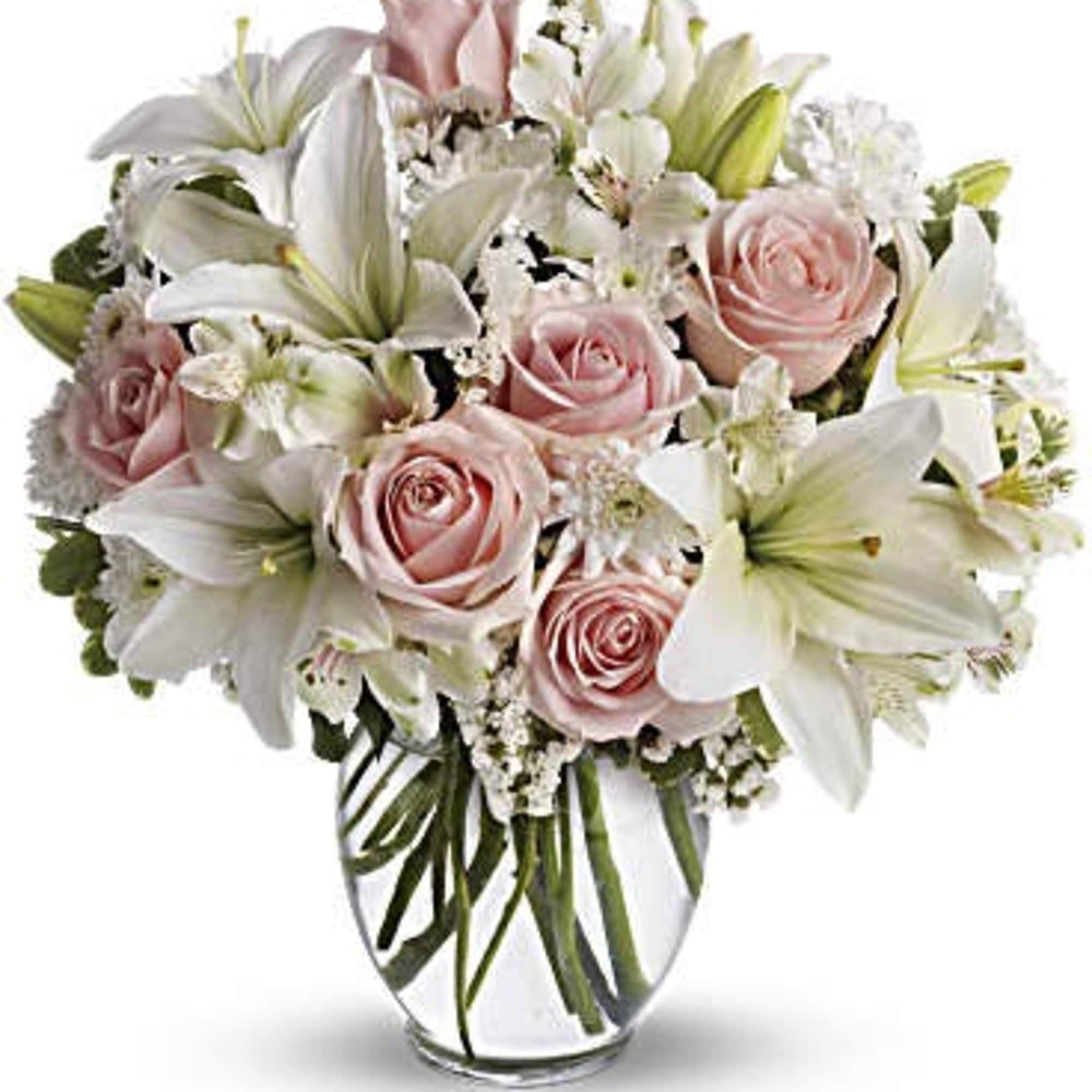 Round arrangement of white lilies and pale pink roses in a clear glass vase