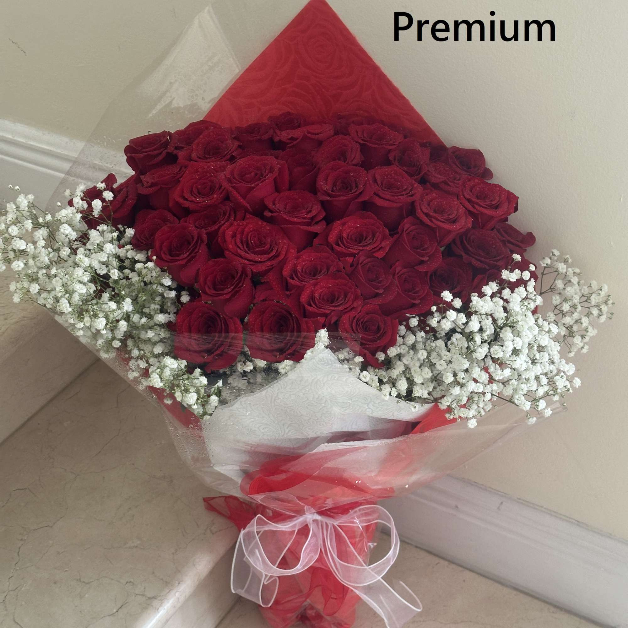 Premium bouquet of red roses with white baby's breath wrapped in clear cellophane and red paper.