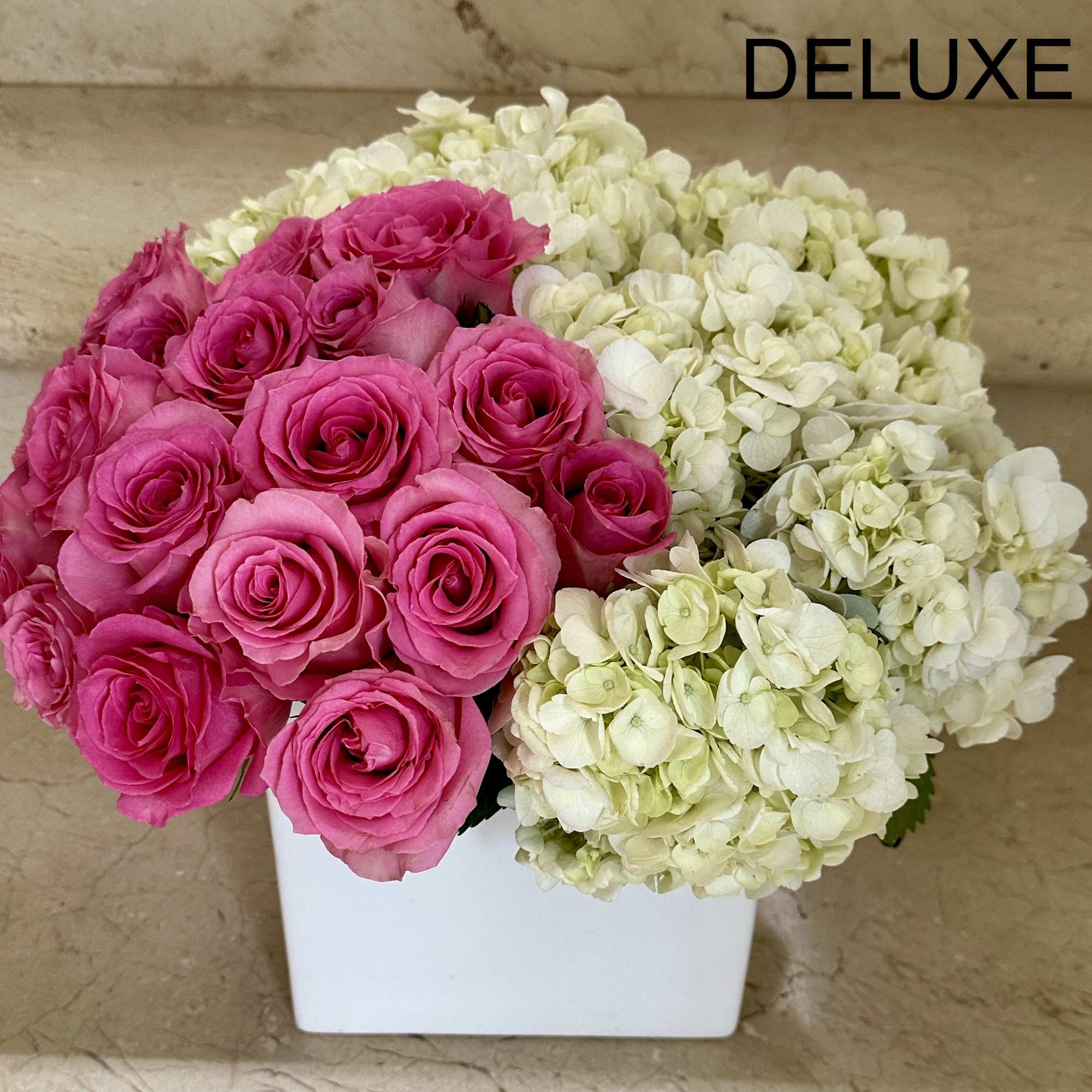 Compact arrangement of hot pink roses and white hydrangeas in a white cube vase