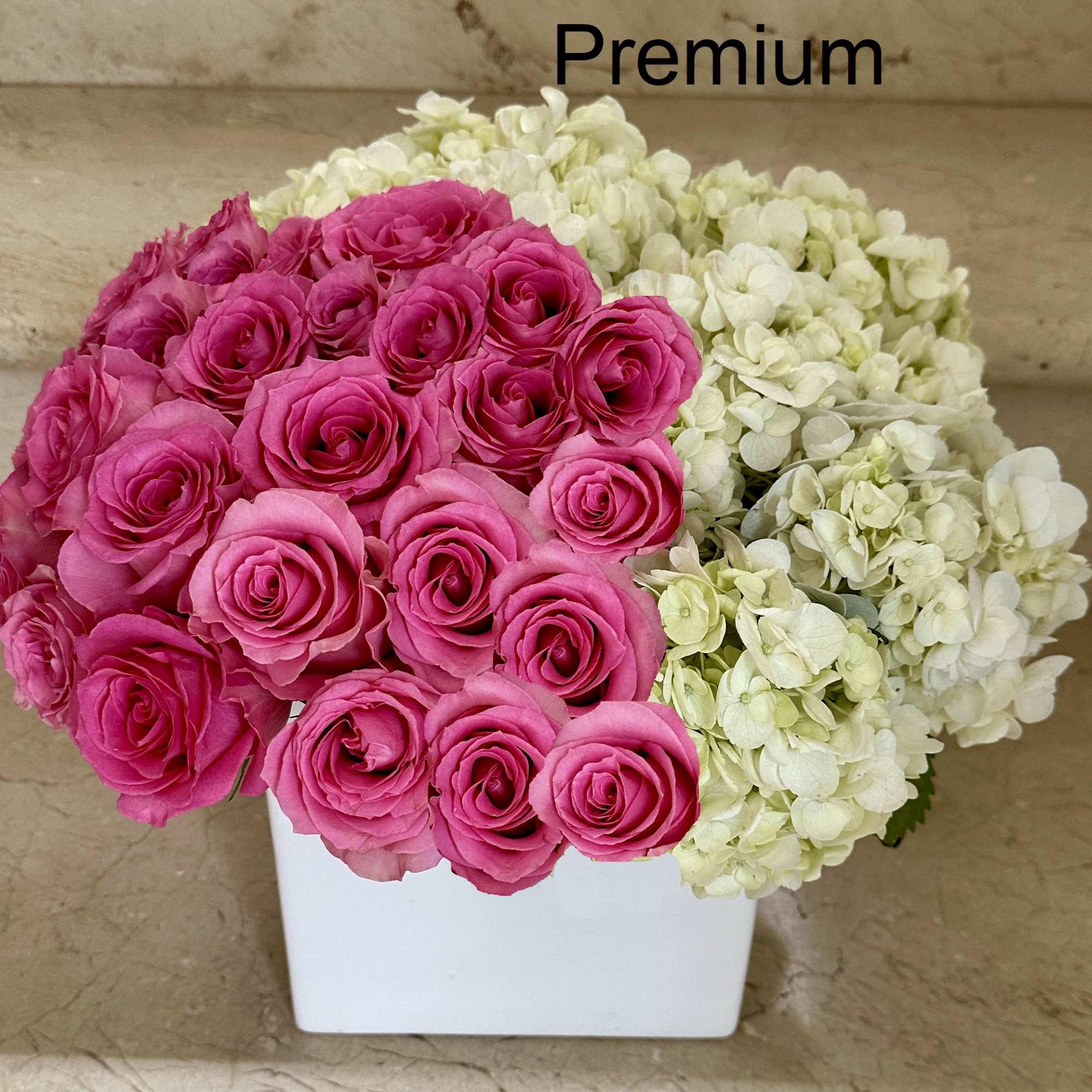 Compact arrangement of bright pink roses and white hydrangeas in a white cube vase