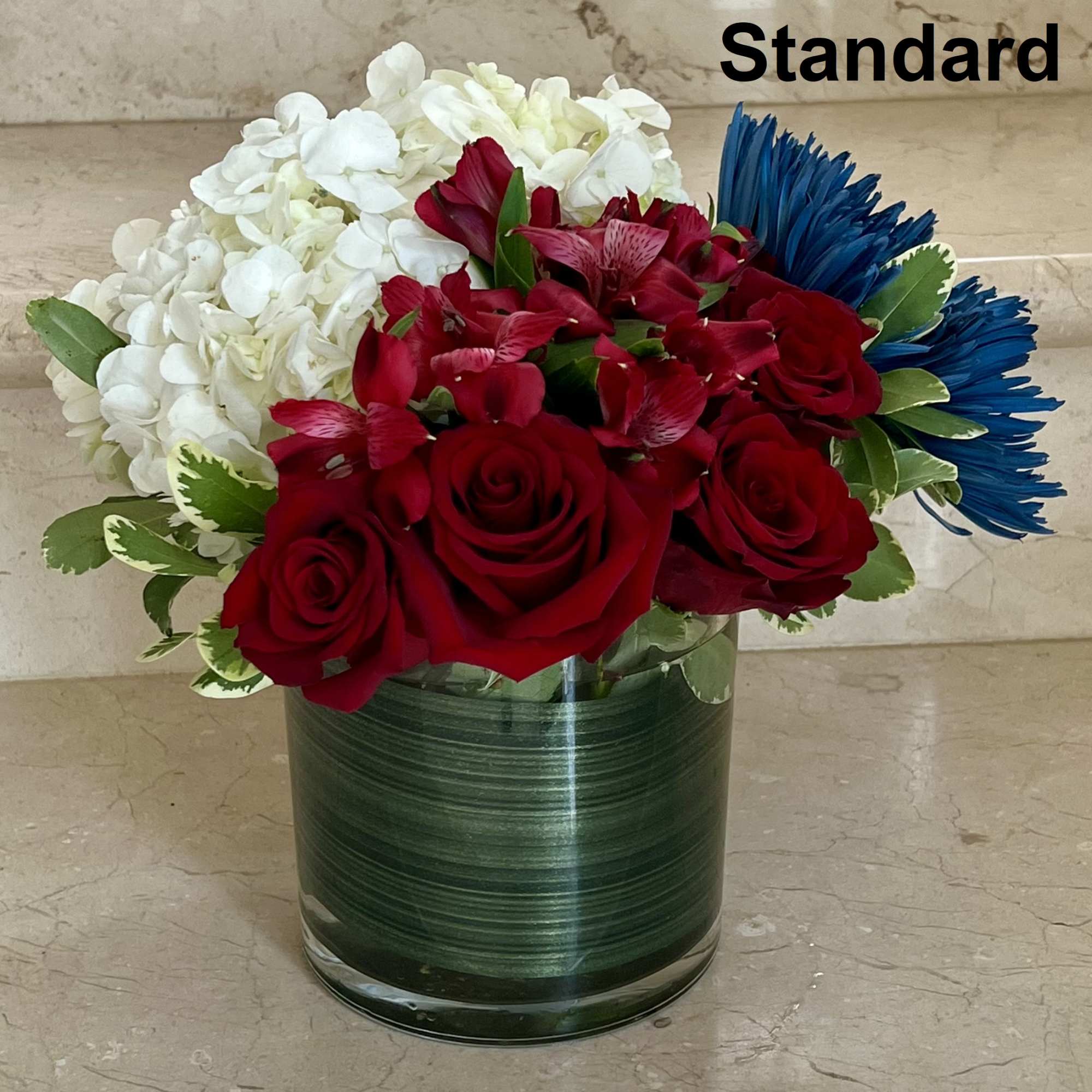 Red roses, white hydrangeas, and blue daisies in a glass vase