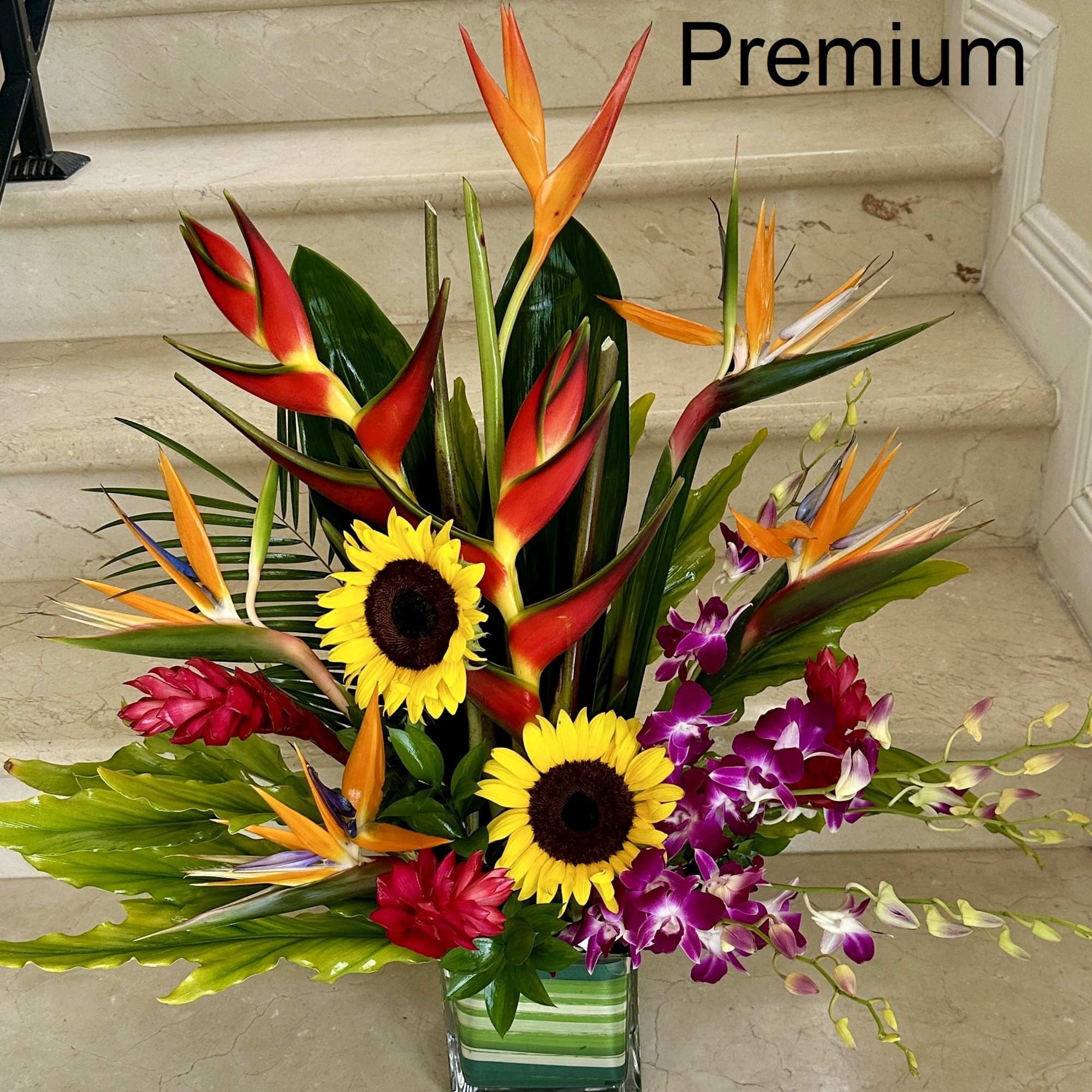 Tall tropical arrangement with birds of paradise, sunflowers, and purple orchids in a clear glass vase