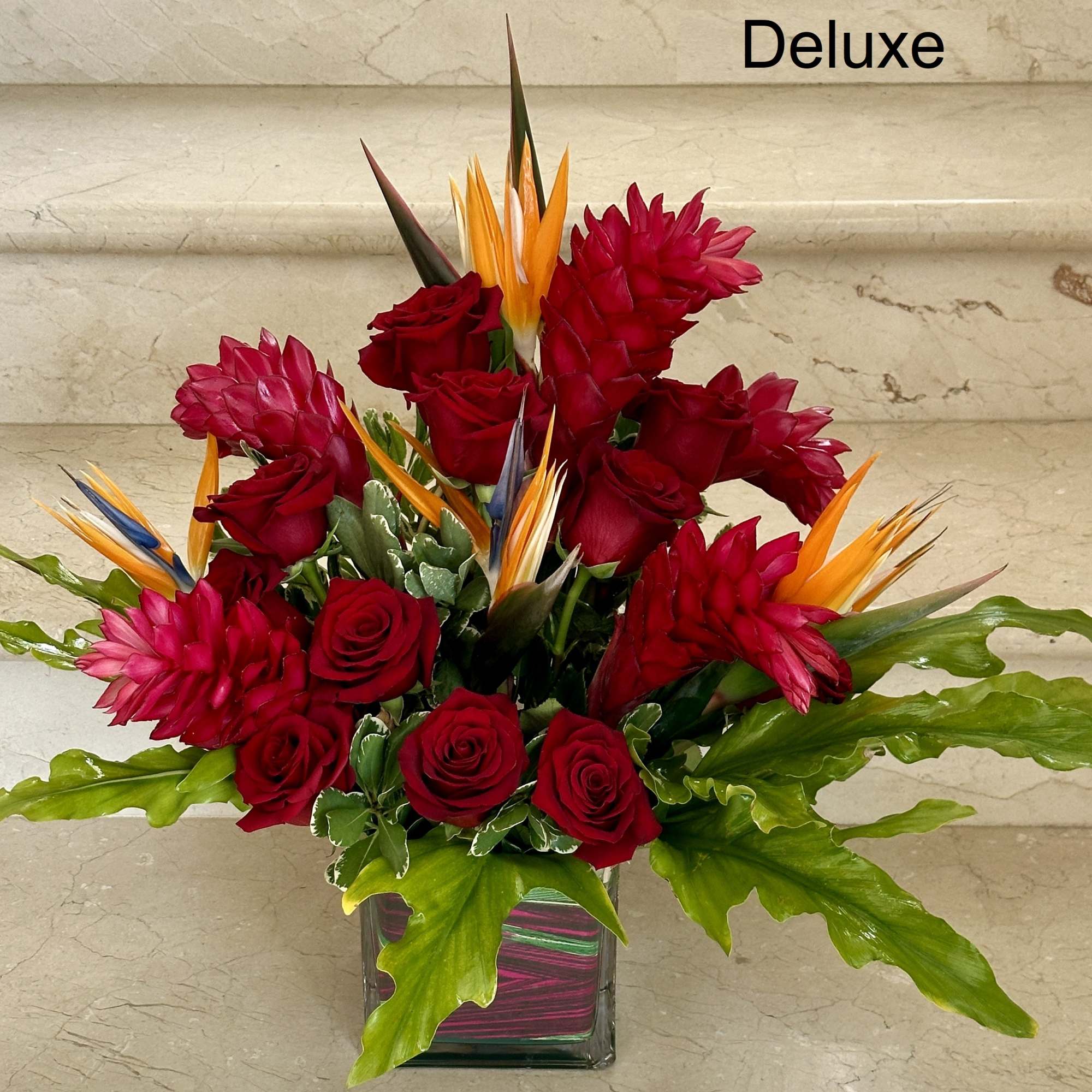 Deluxe arrangement of red roses with tropical orange blooms in a square glass vase