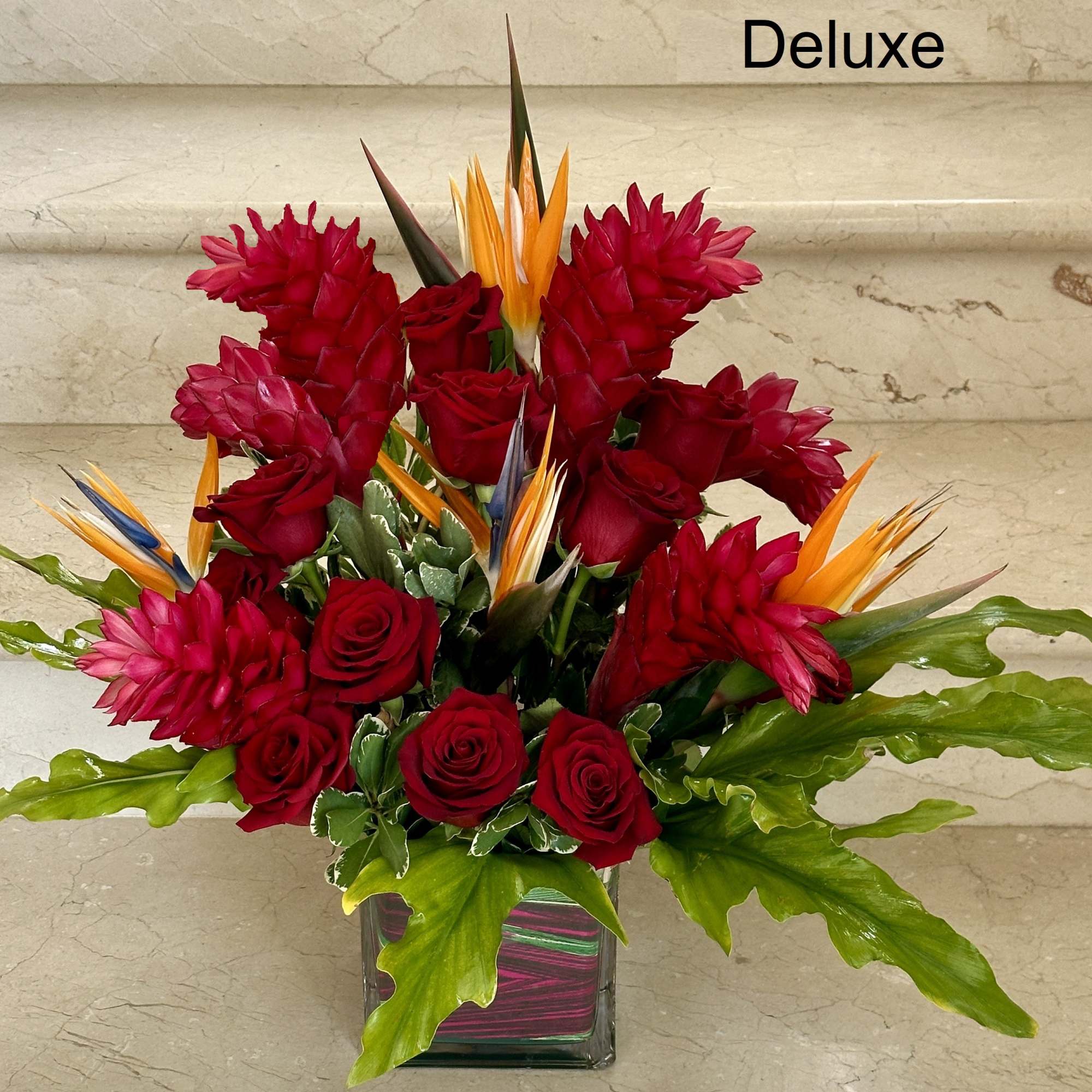 Deluxe arrangement of red roses and tropical flowers in a square glass vase