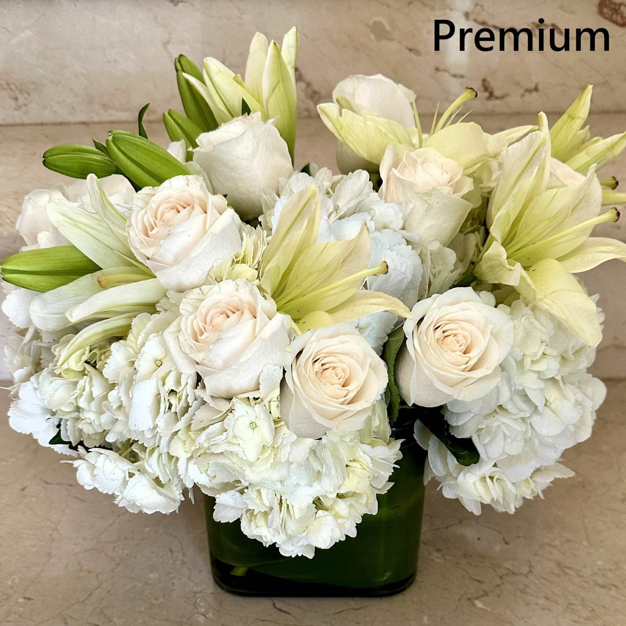 Compact white roses, lilies, and hydrangeas arranged in a green glass cube vase