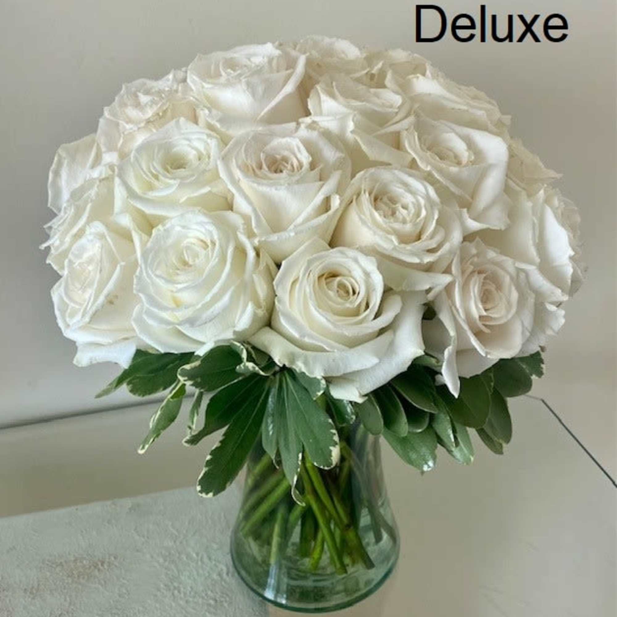 Deluxe arrangement of white roses tightly clustered in a clear glass vase