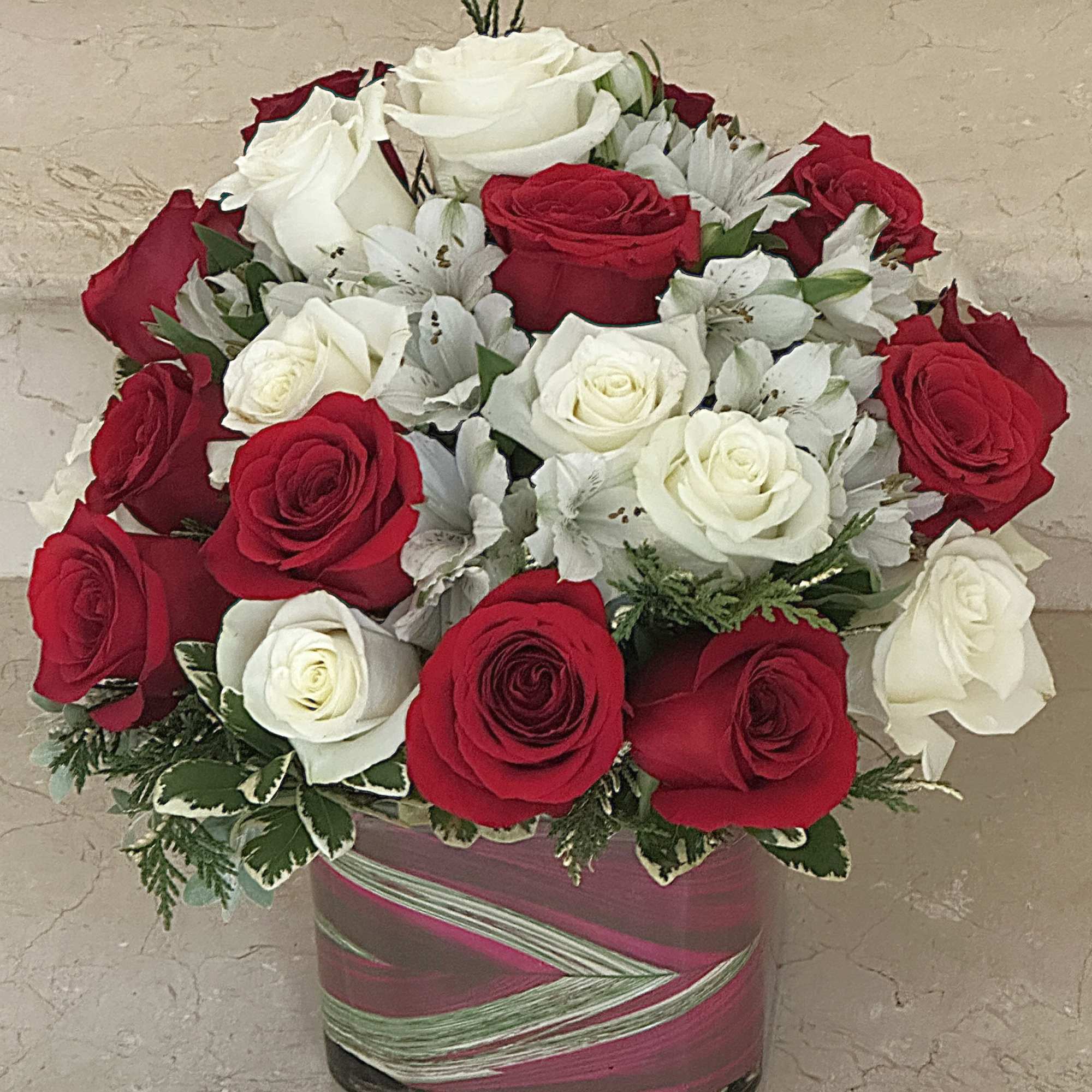 Arrangement of red and white roses with white accent flowers in a square glass vase