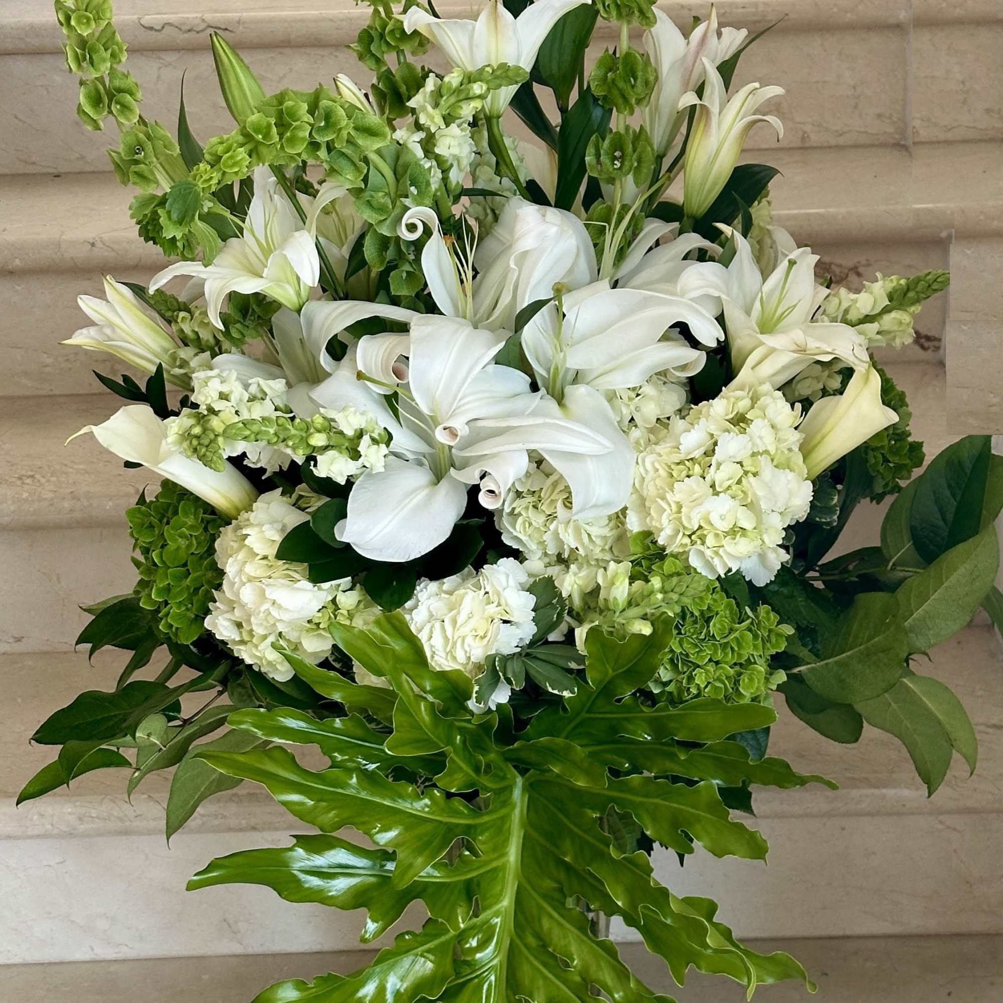 Tall white lily and hydrangea arrangement with green bells of Ireland and large tropical foliage