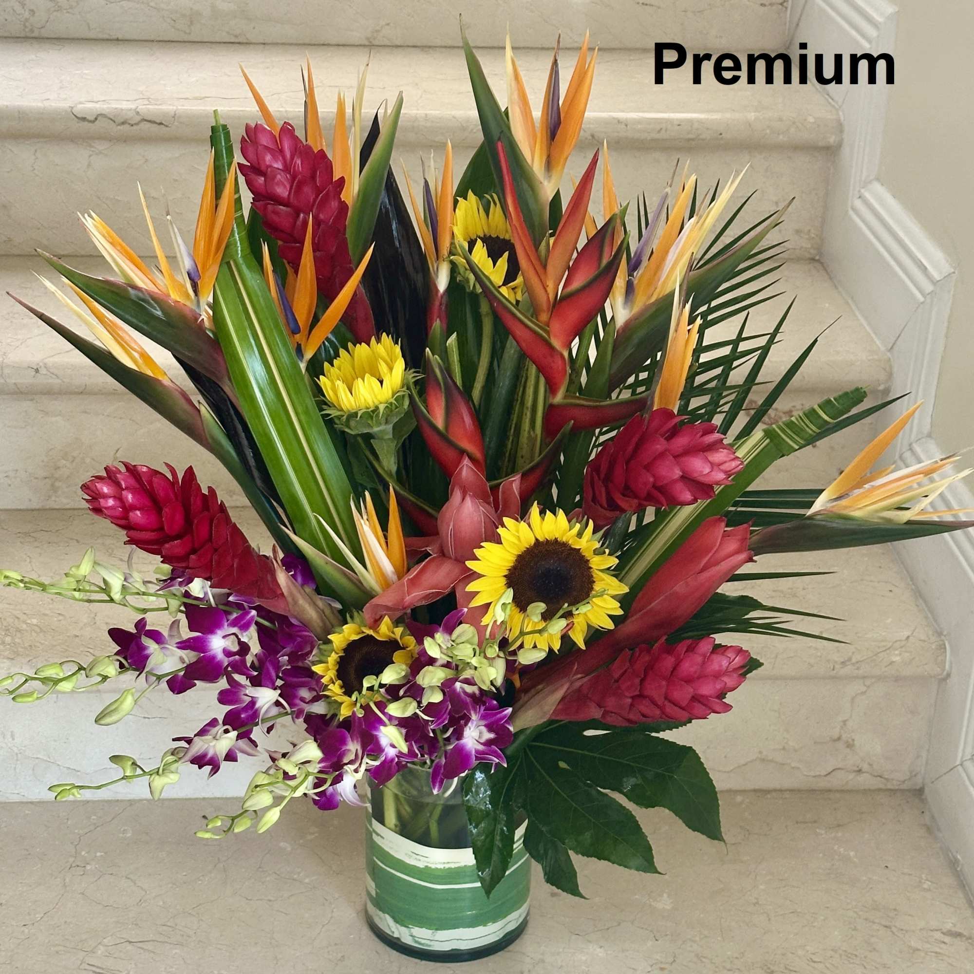 Tall tropical arrangement with red gingers, birds of paradise, sunflowers, and orchids in a glass vase