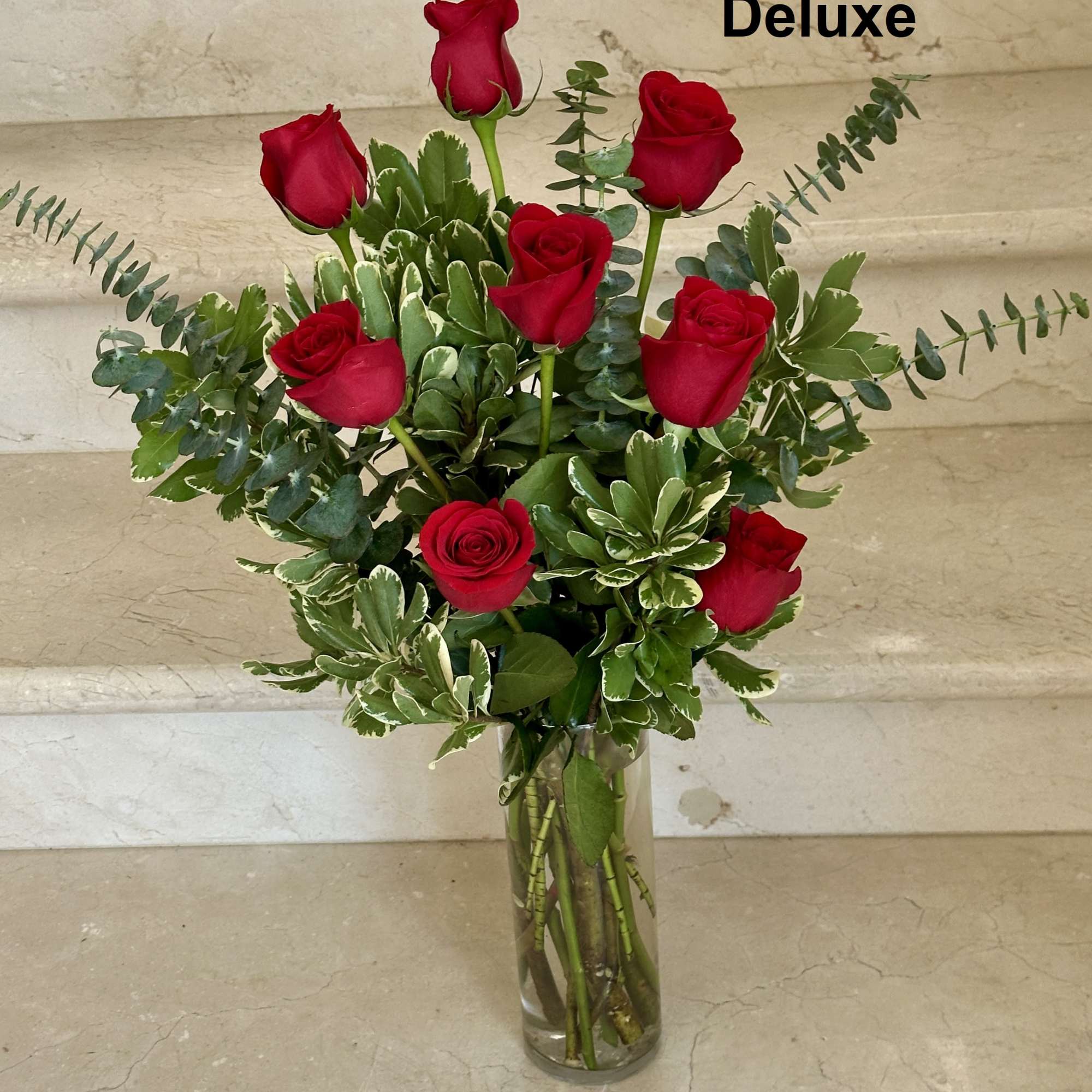 Tall arrangement of red roses with variegated foliage in a clear glass vase