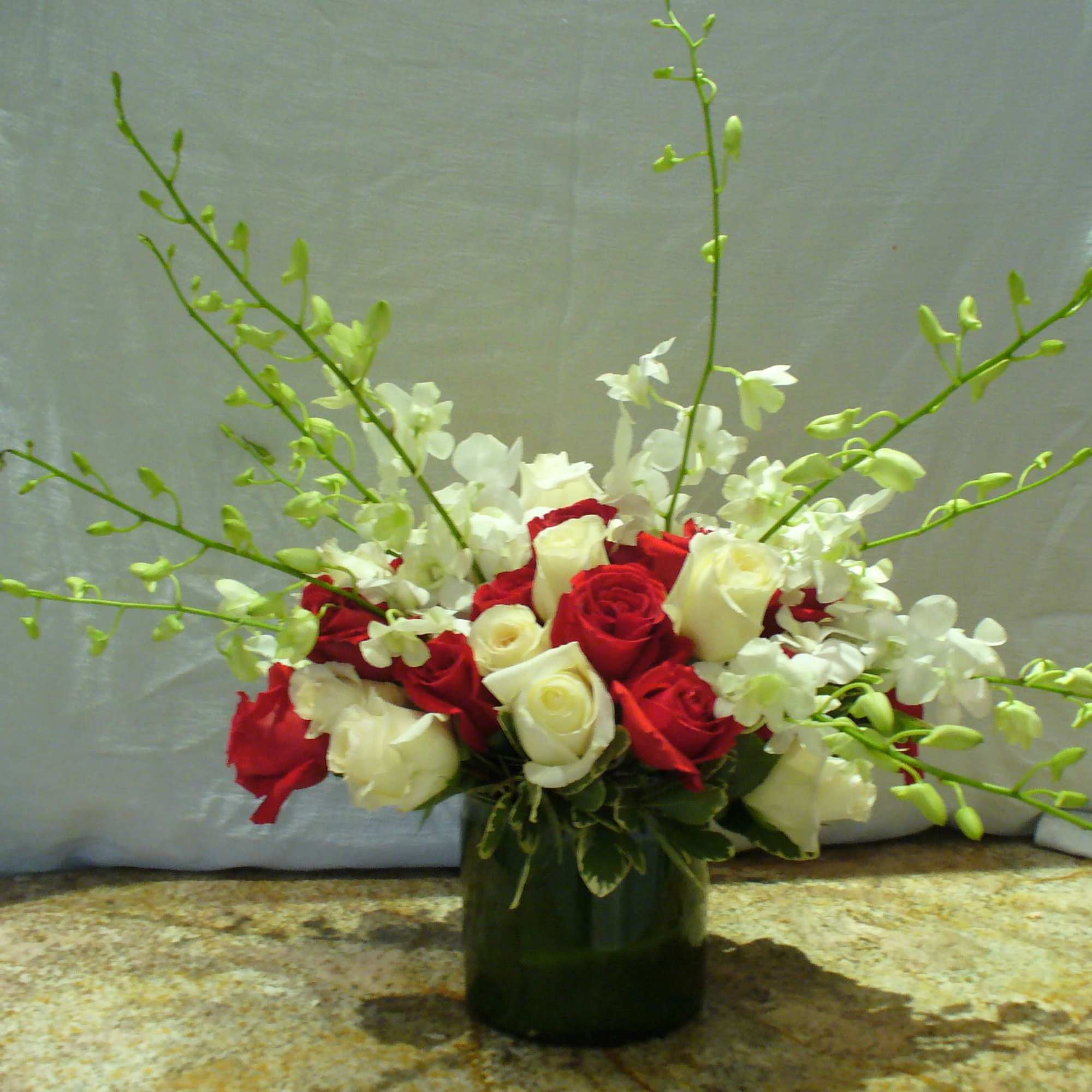 Low red and white rose arrangement with white orchids in a green glass vase
