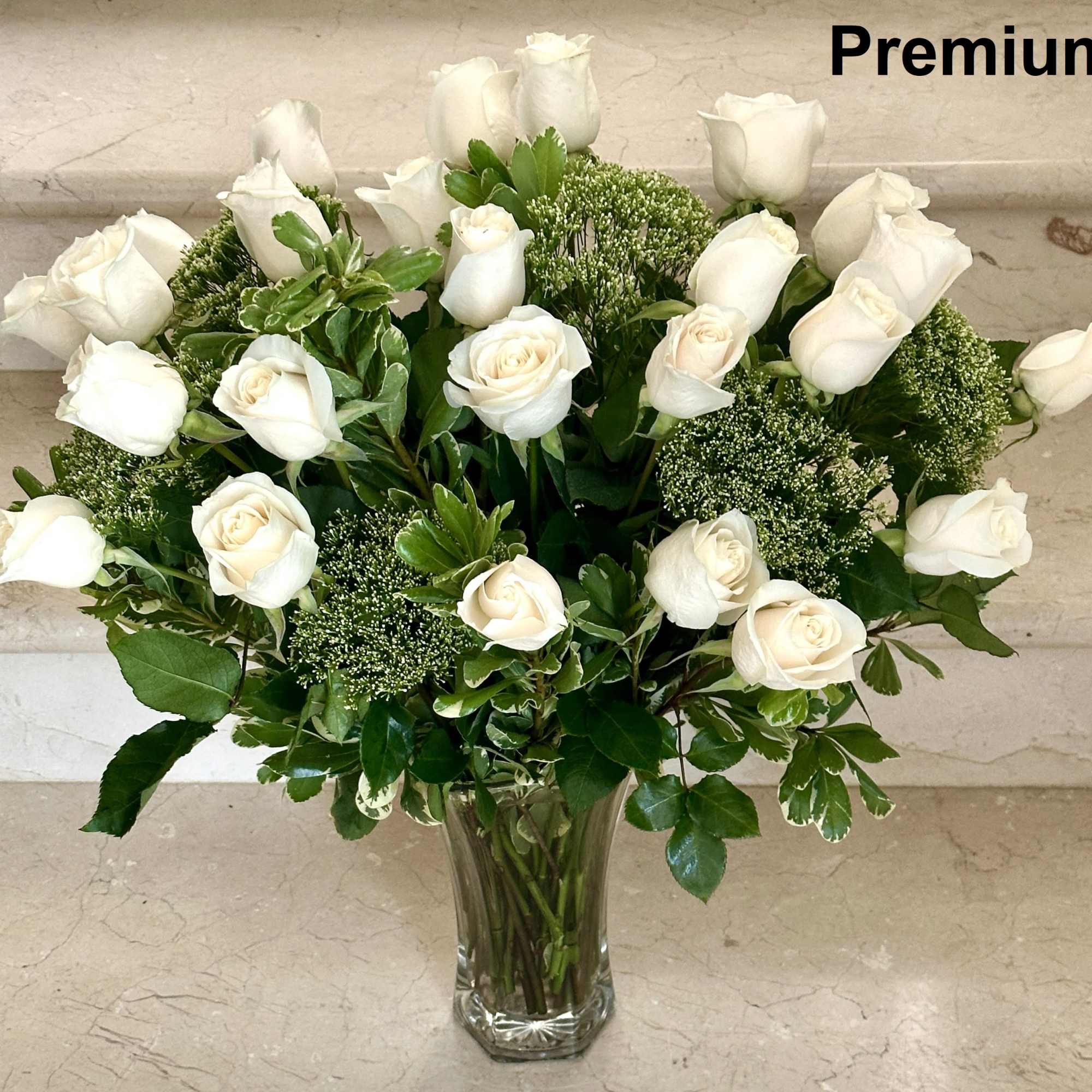 Tall arrangement of white roses in a clear glass vase with lush filler.