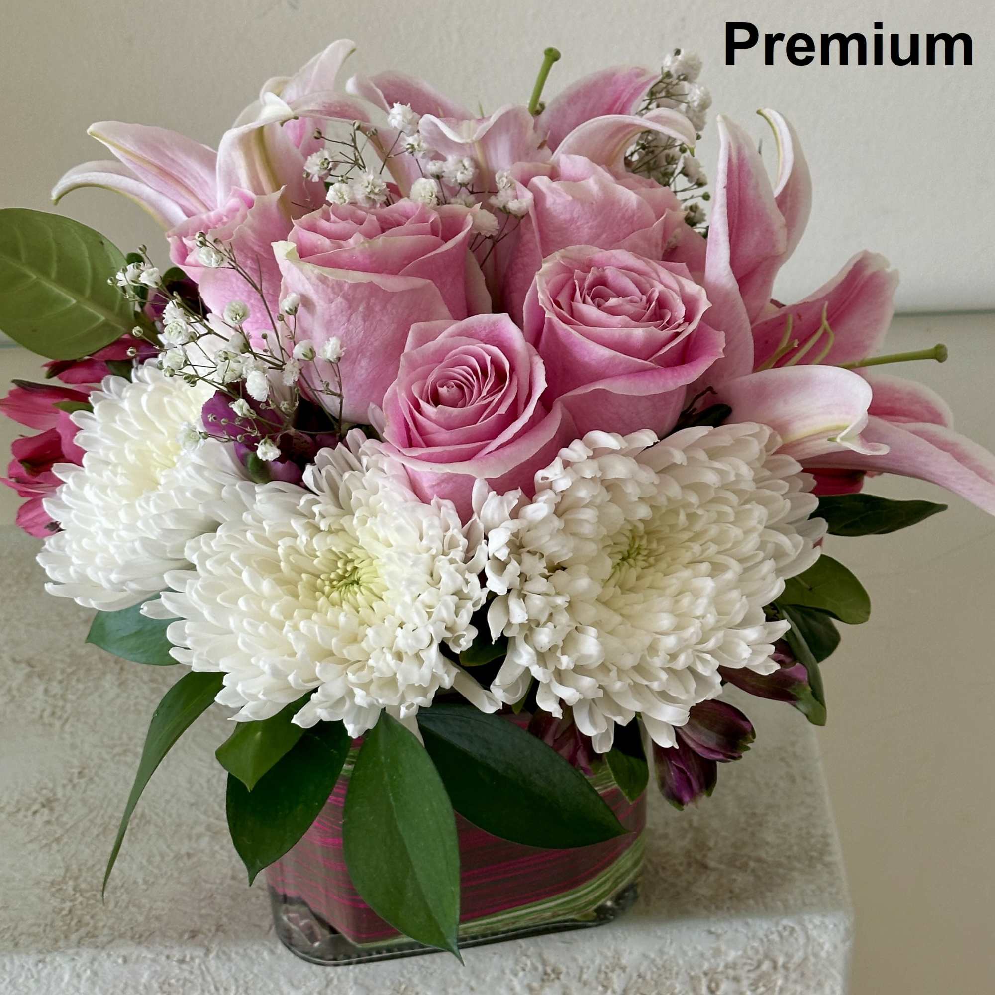 Compact arrangement of pink roses, pink lilies, and white chrysanthemums in a glass cube vase