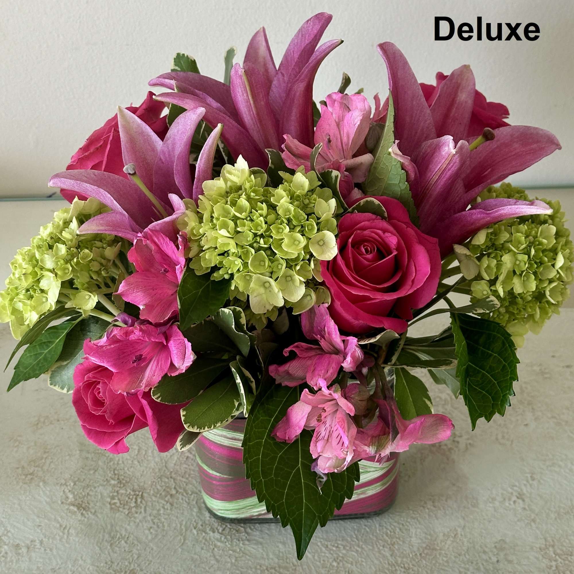 Low cube arrangement of pink lilies, roses, and green hydrangeas in a striped glass vase.