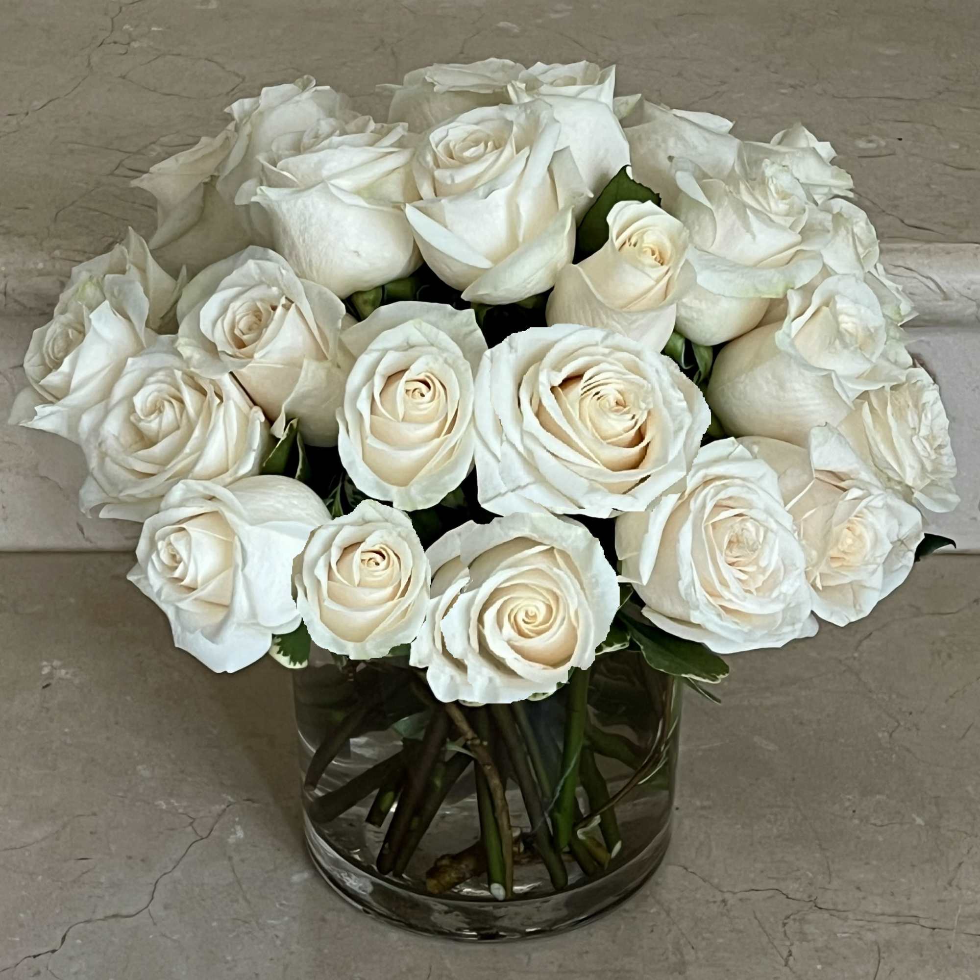 Compact arrangement of ivory white roses in a clear glass cylinder vase