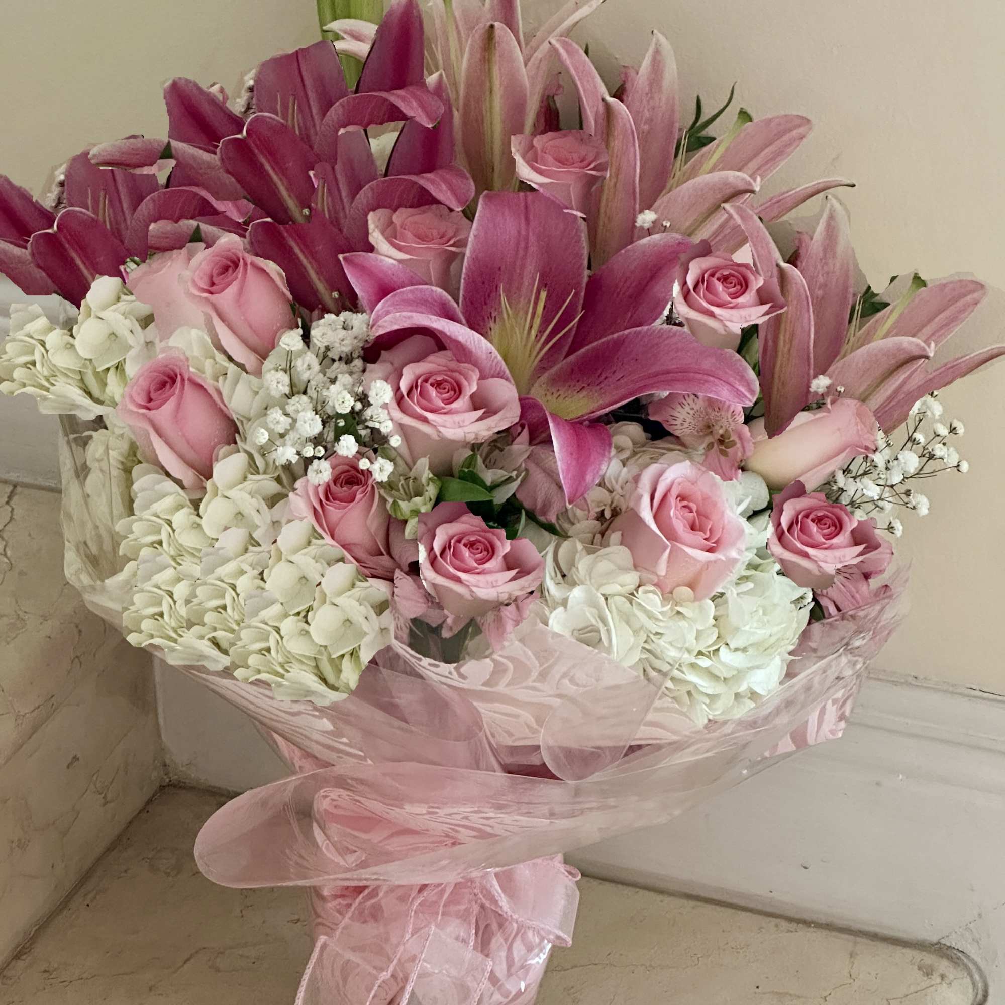 Large pink and white bouquet with lilies, roses, and hydrangeas wrapped in pink cellophane