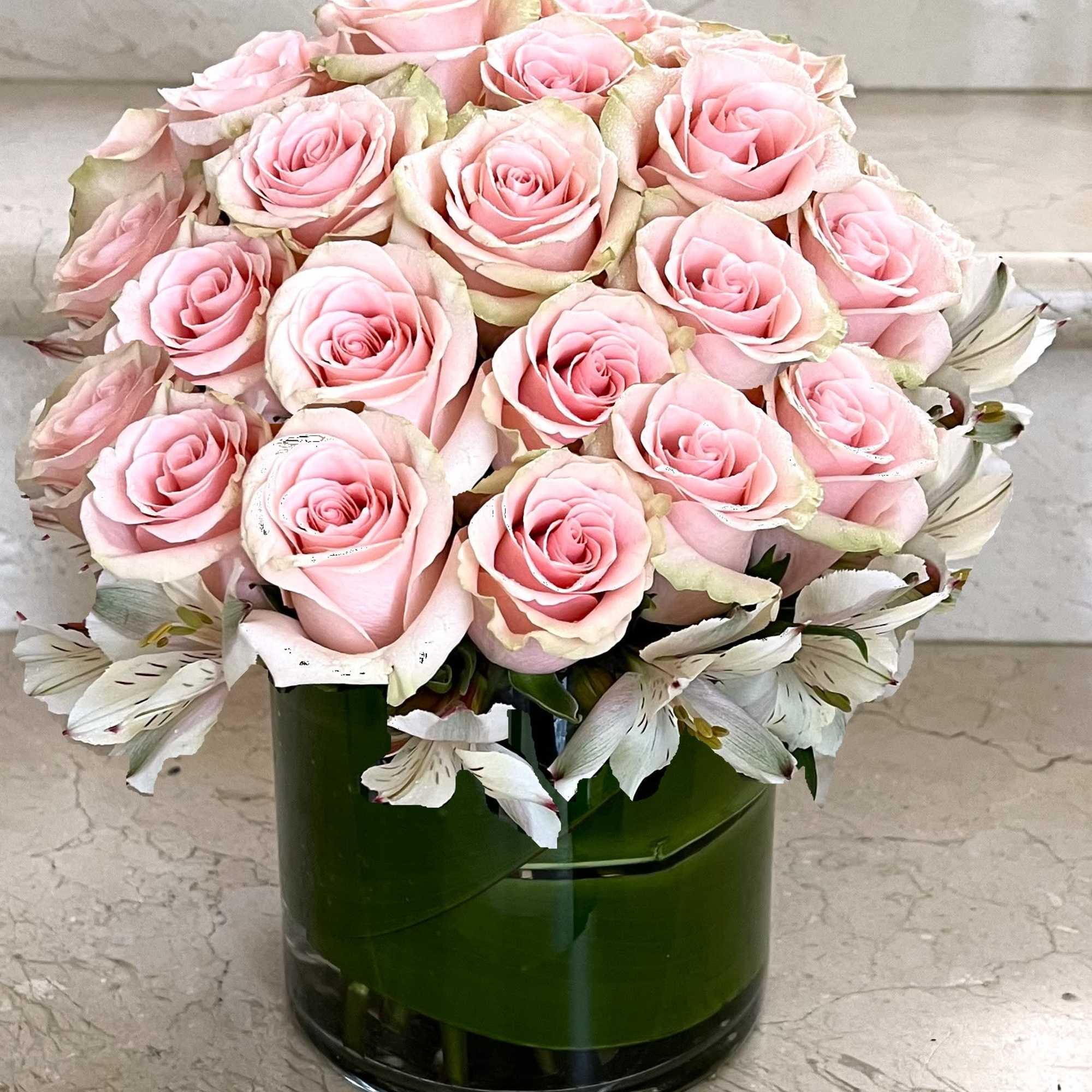 Pink roses arranged in a green glass vase with white flowers around the base