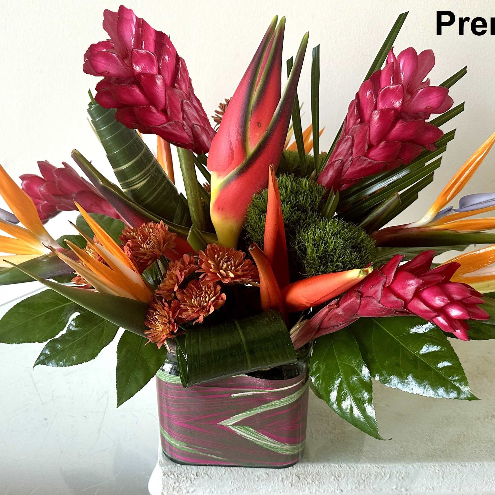 Tropical arrangement with orange birds of paradise and red ginger in a square vase.