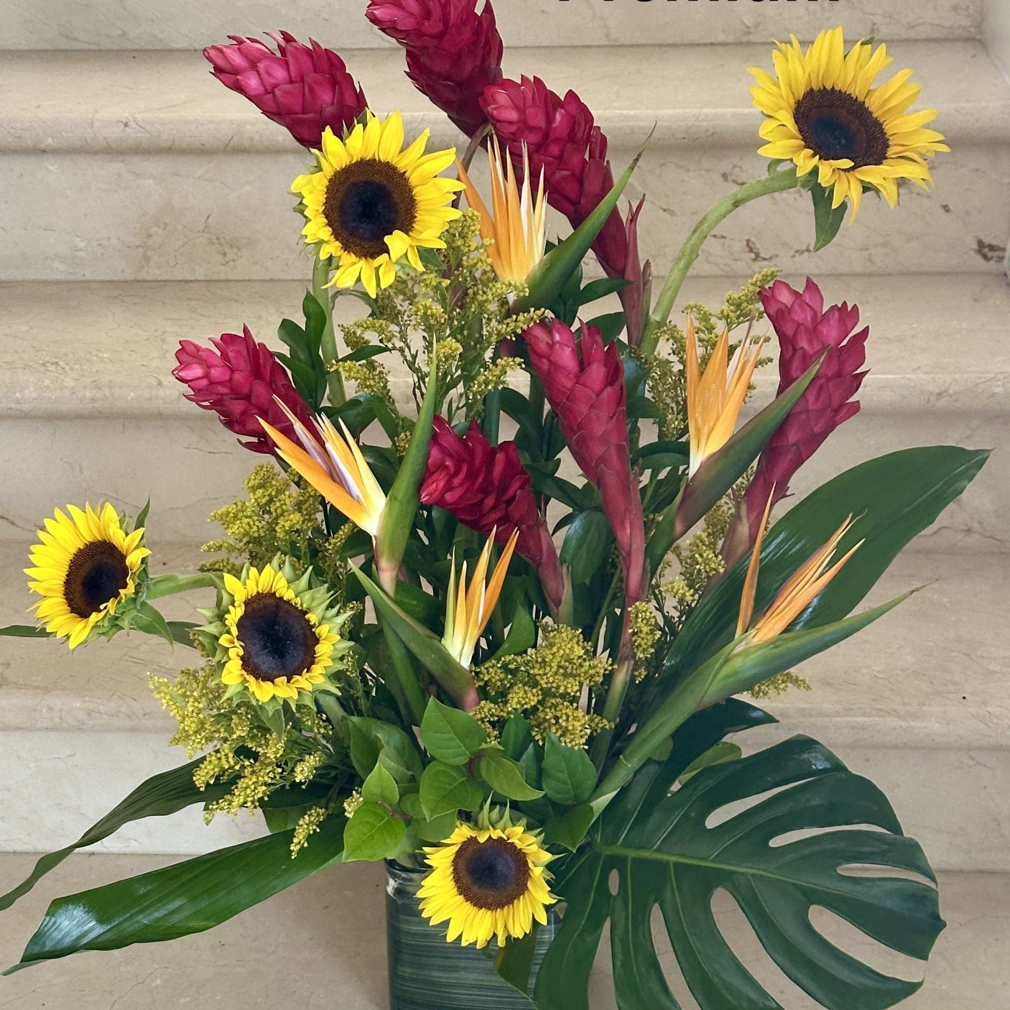 Tropical arrangement with sunflowers, pink ginger, and bird of paradise in a vase
