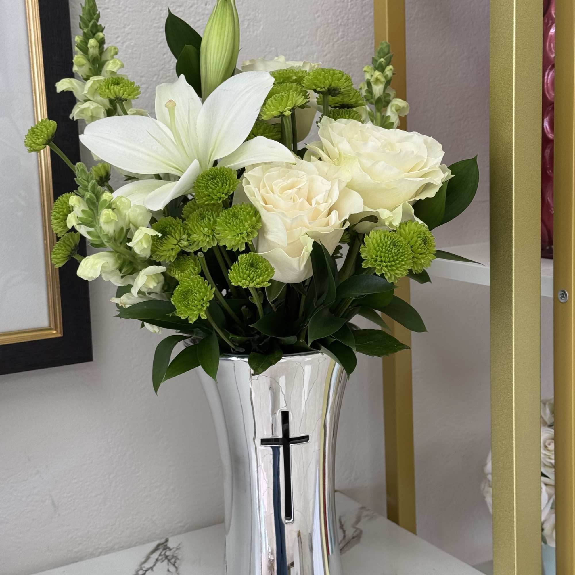 White lilies and roses in a silver vase with a cross