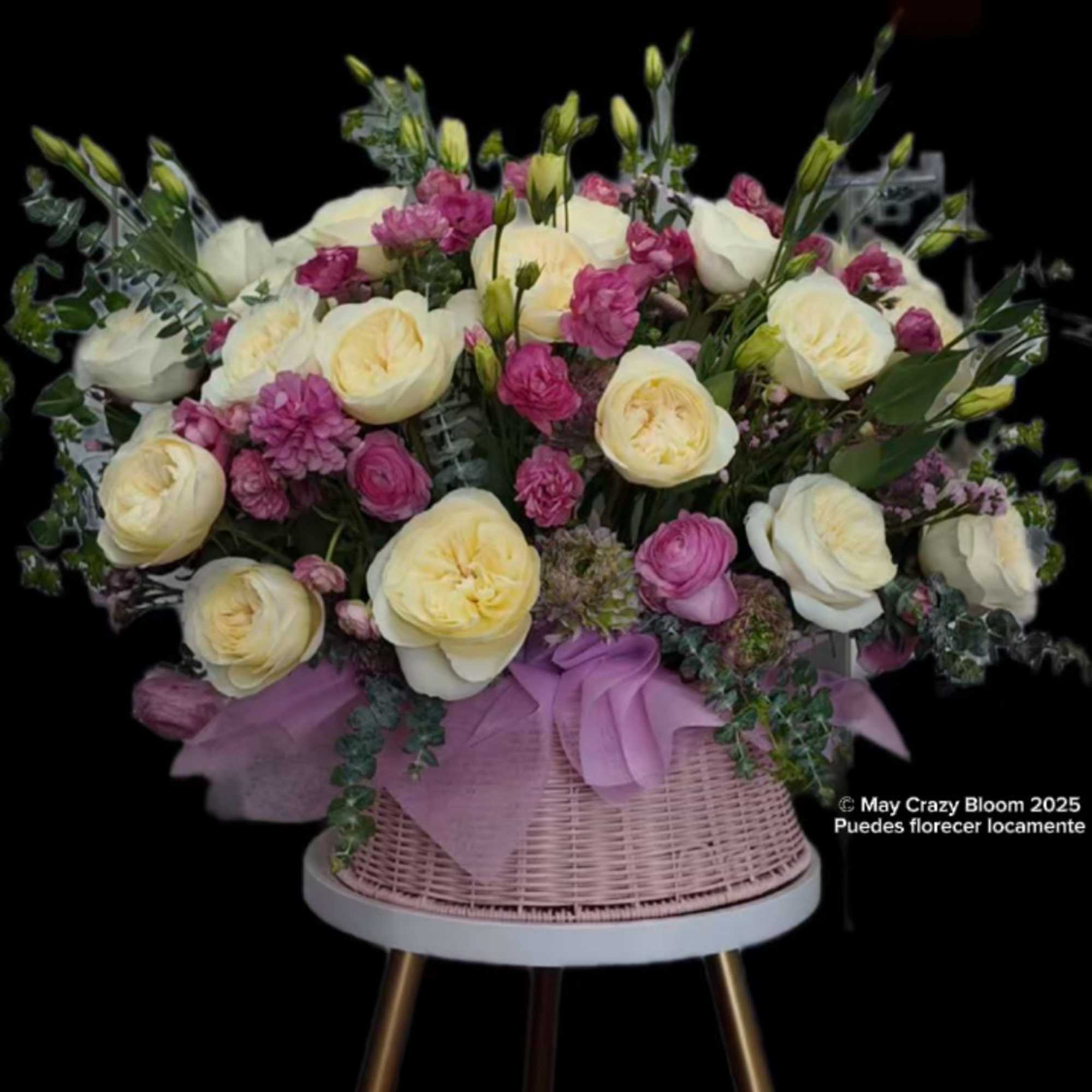 Pink and cream roses arranged in a wicker basket with a lavender ribbon.