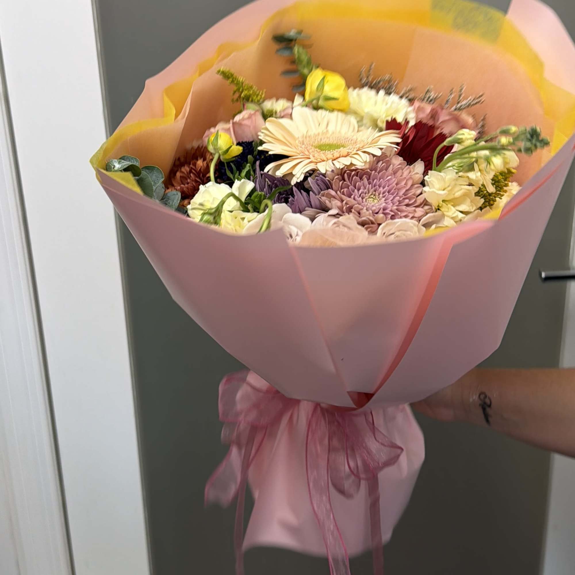 Handheld bouquet of mixed pastel flowers wrapped in pink paper