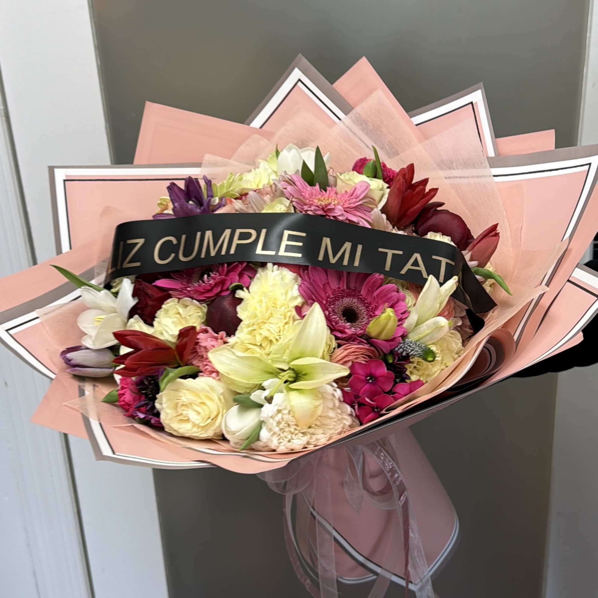 Mixed bouquet of pink, red, white, and yellow flowers wrapped in pink paper