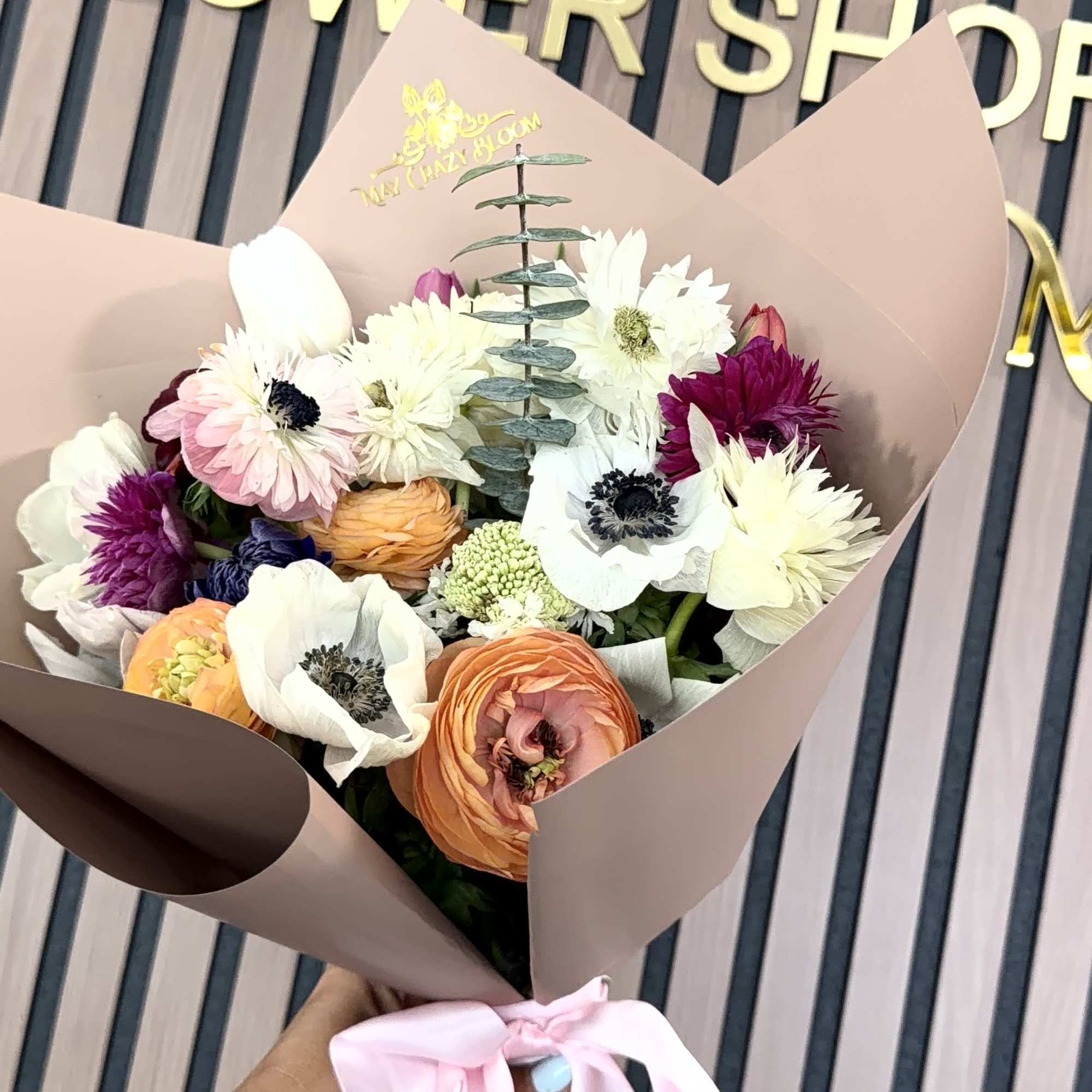 A rounded hand-tied bouquet of anemone, ranunculus, tulips and daisy-like blooms in