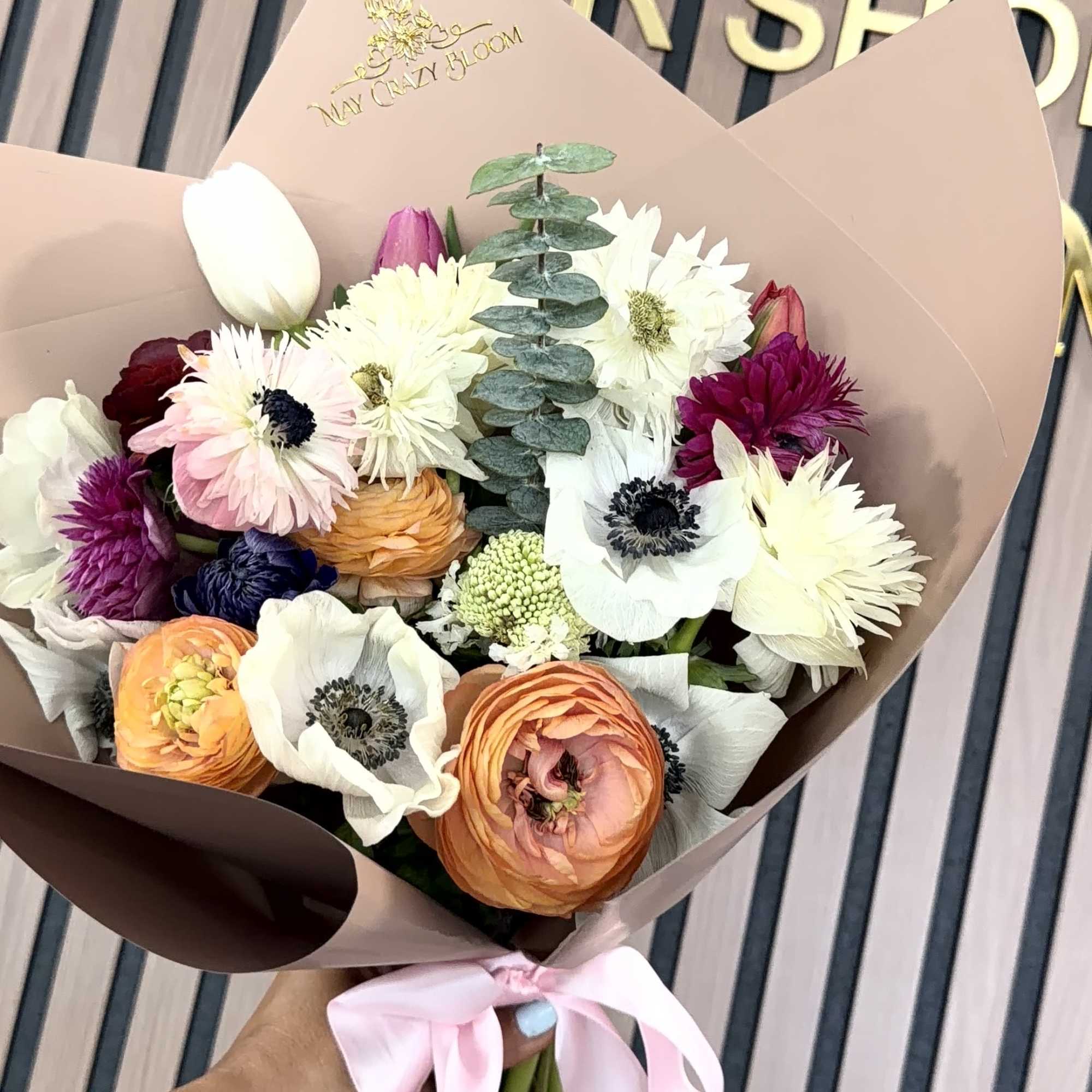 A rounded hand-tied bouquet of anemone, ranunculus, tulips and daisy-like blooms in, photo 2 of 2