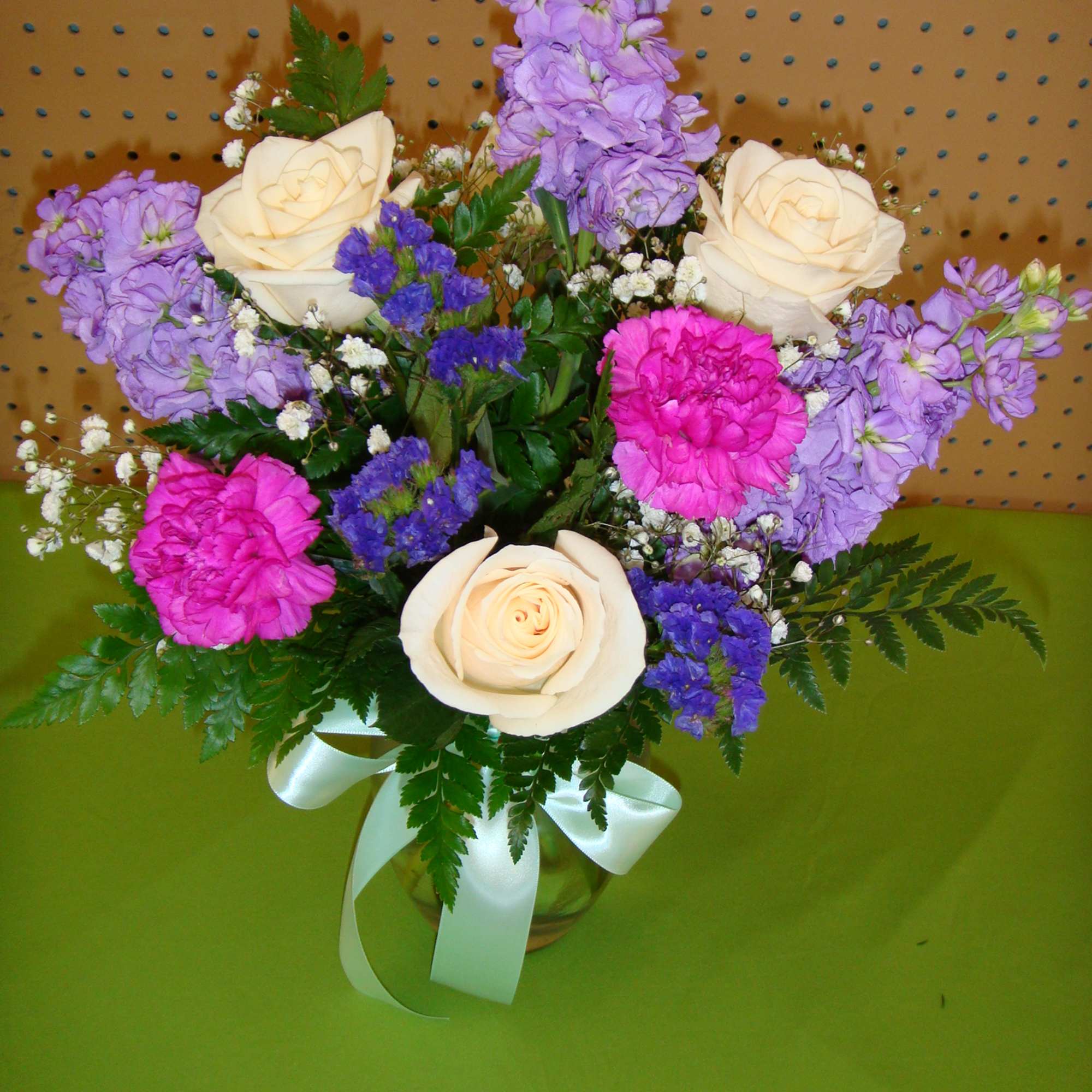 Bouquet of cream roses, pink carnations, and purple flowers in a glass vase