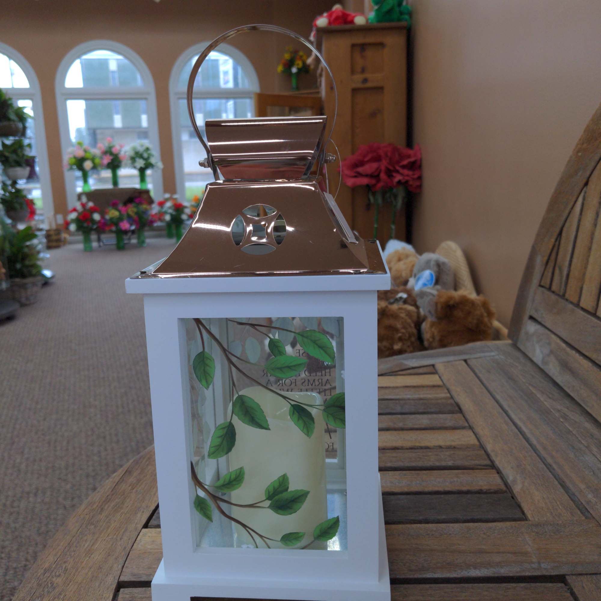 White lantern with copper top and leaf design glass panels holding a cream pillar candle