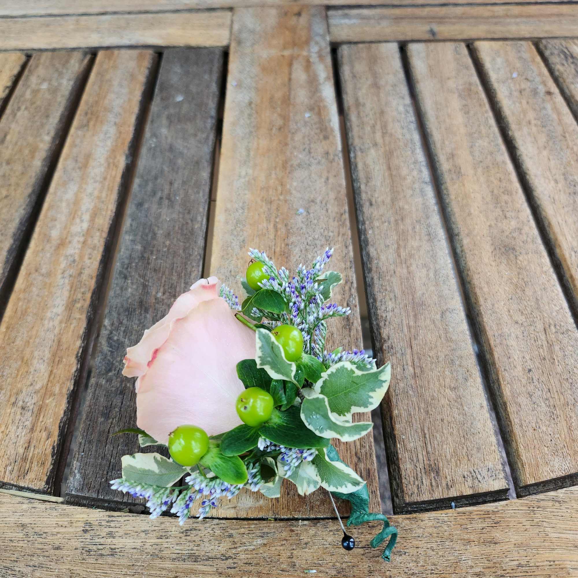 A pale pink rose boutonniere with small purple filler flowers and green berries.