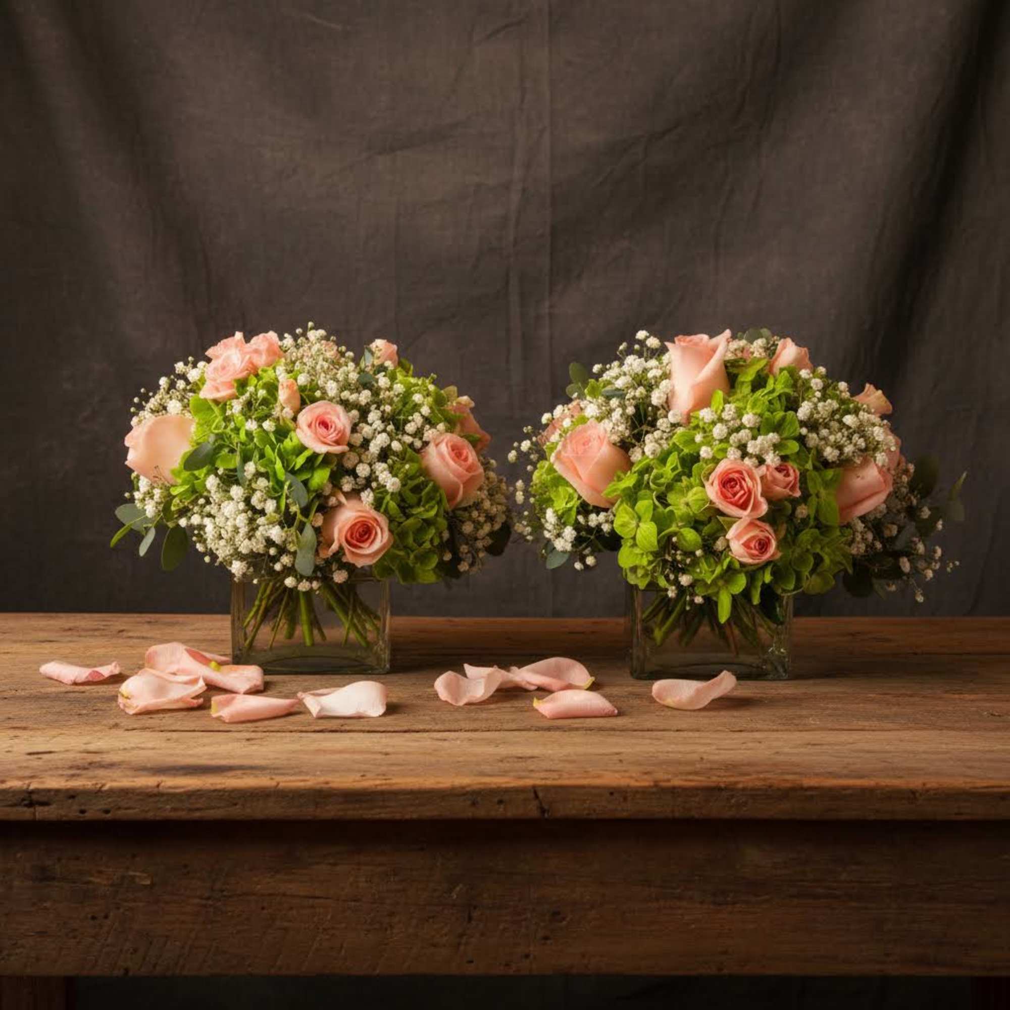 Two pink rose arrangements in square glass vases on a wooden table