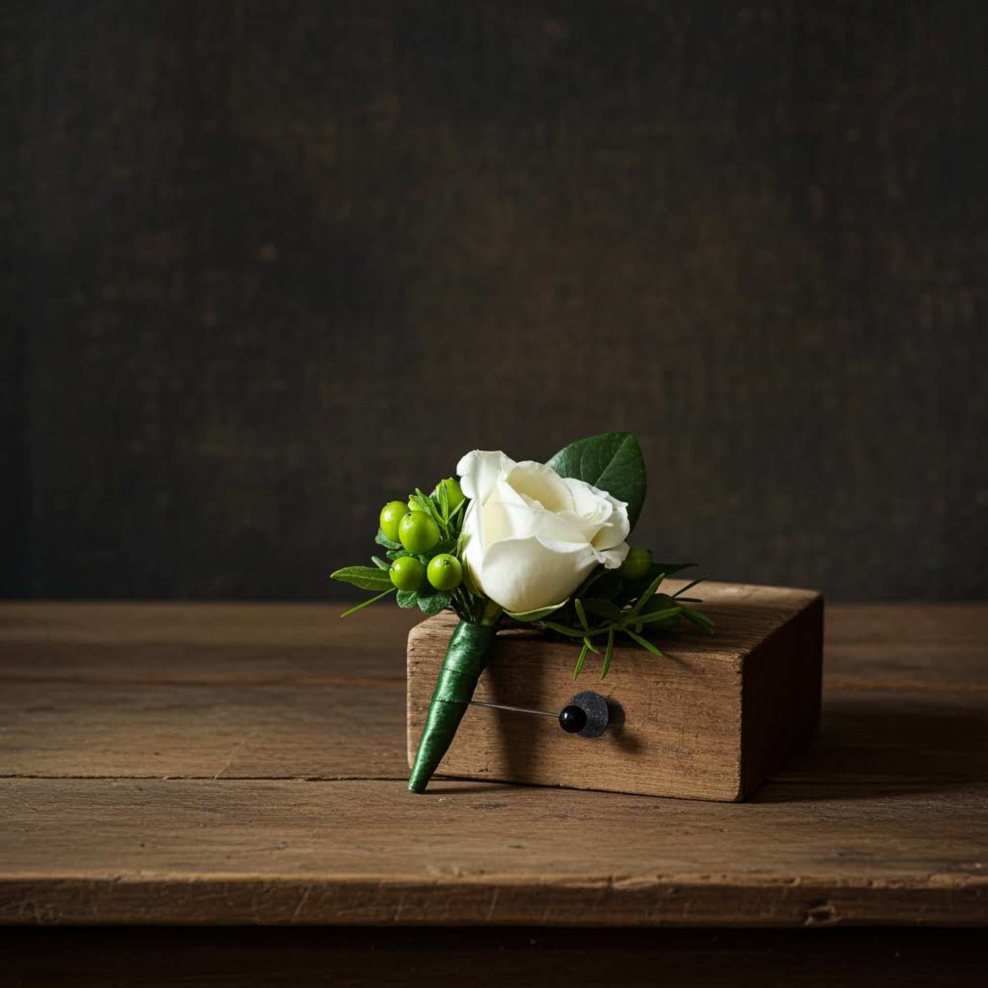 White rose boutonniere with green berries resting on a small wooden block