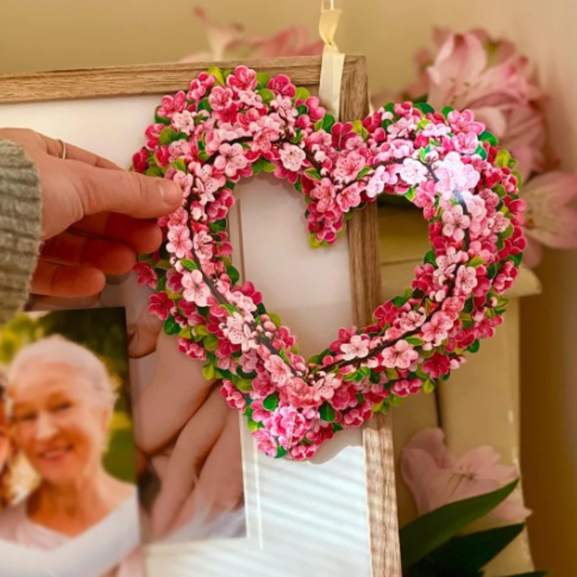 Heart-shaped floral frame with pink blossoms held in a hand