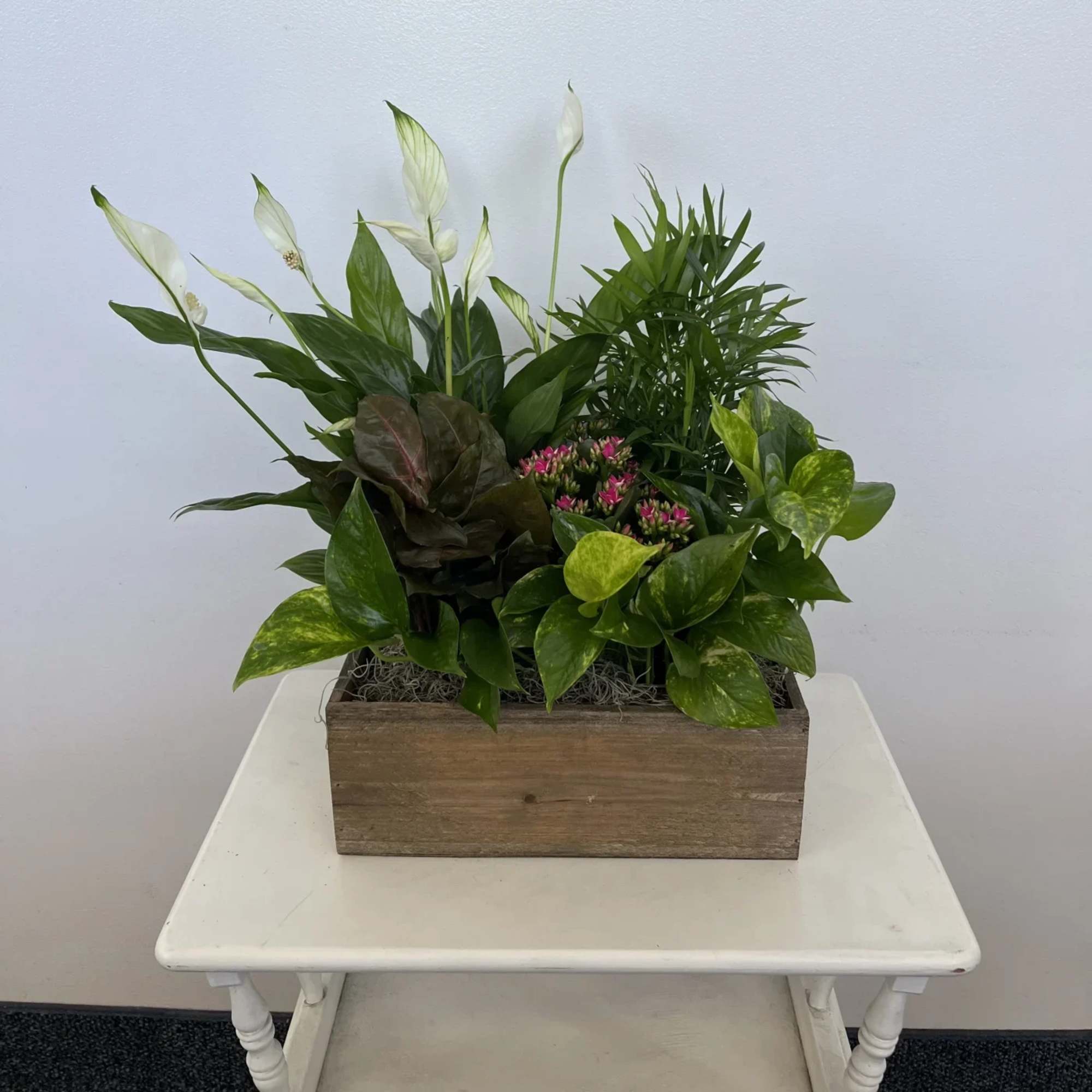 Potted arrangement of white peace lilies and mixed green plants in a wooden box