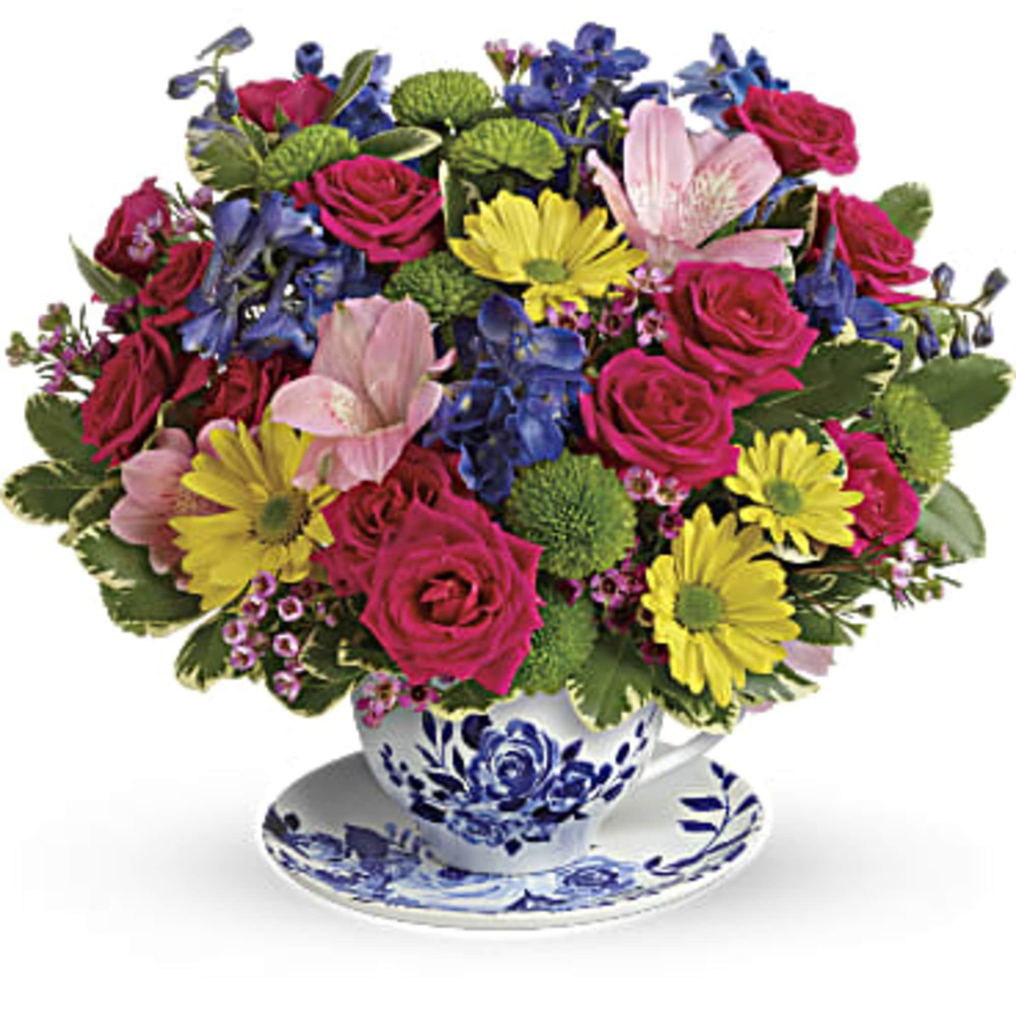Mixed bouquet of pink roses, yellow daisies, and blue flowers in a teacup vase