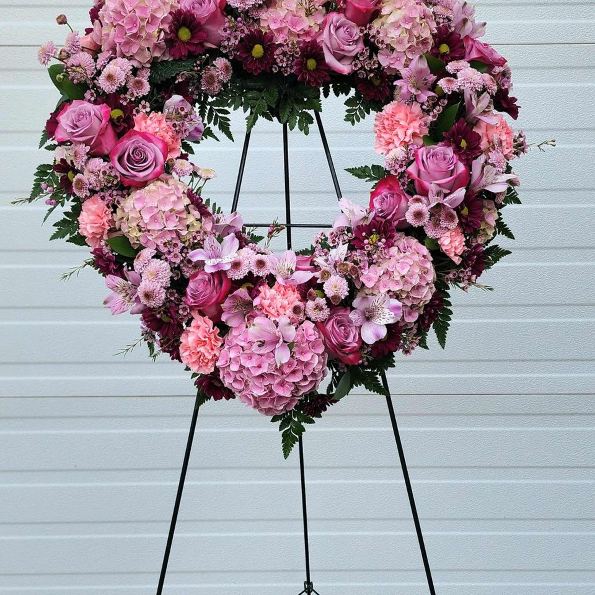 Heart-shaped floral wreath on a black stand with pink and purple blooms