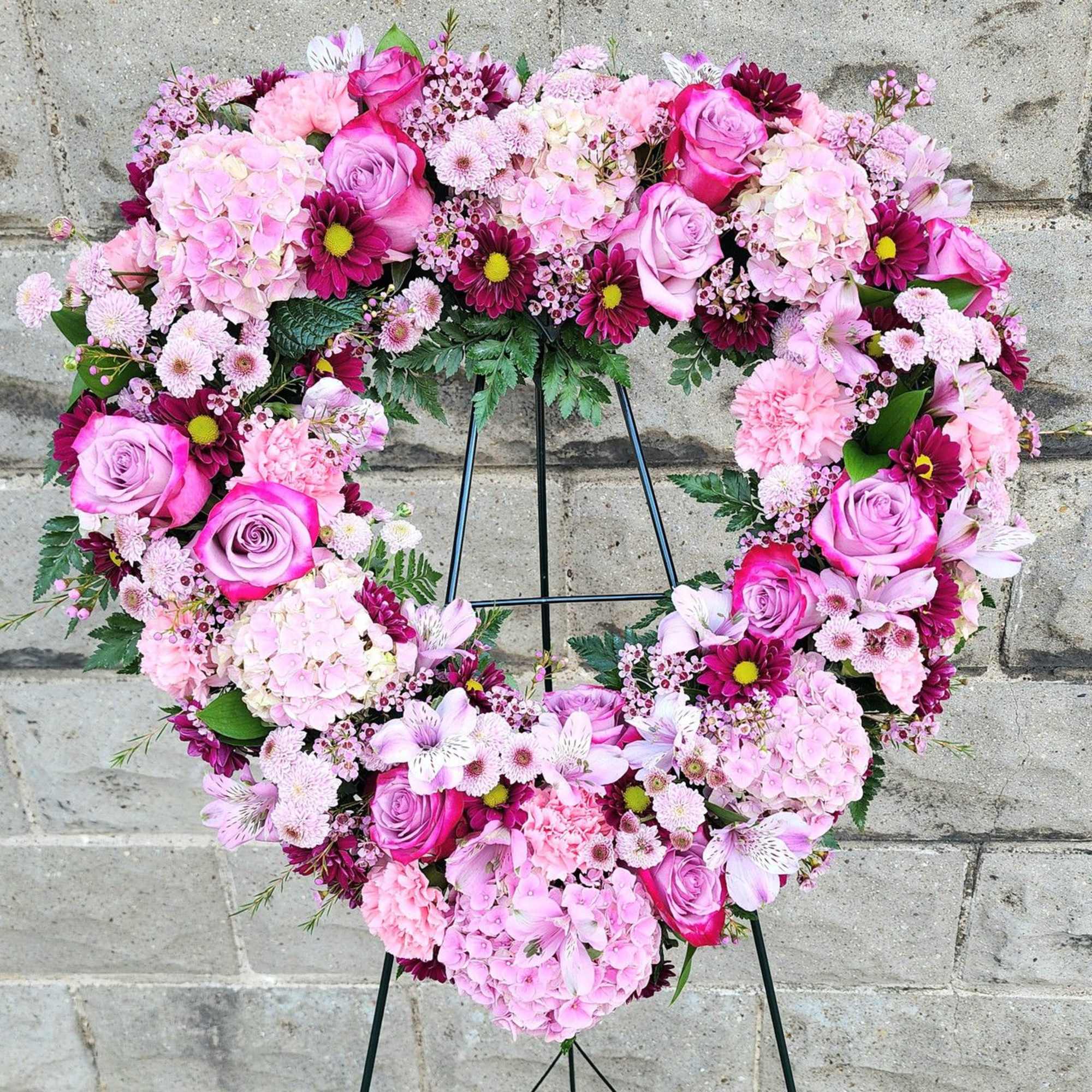 Heart-shaped floral wreath with pink roses and hydrangeas on a black stand