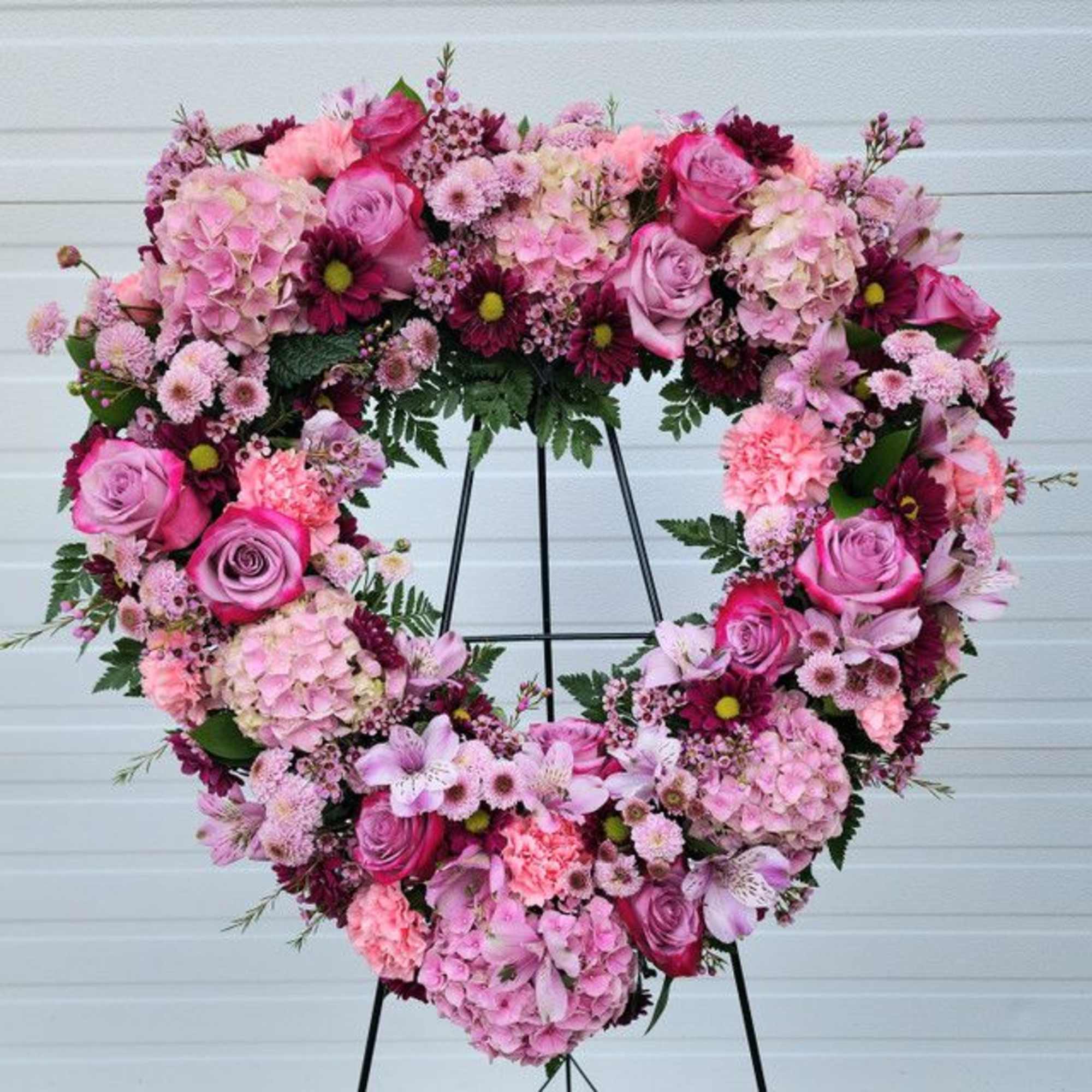 Heart-shaped floral wreath with pink and purple flowers on a stand