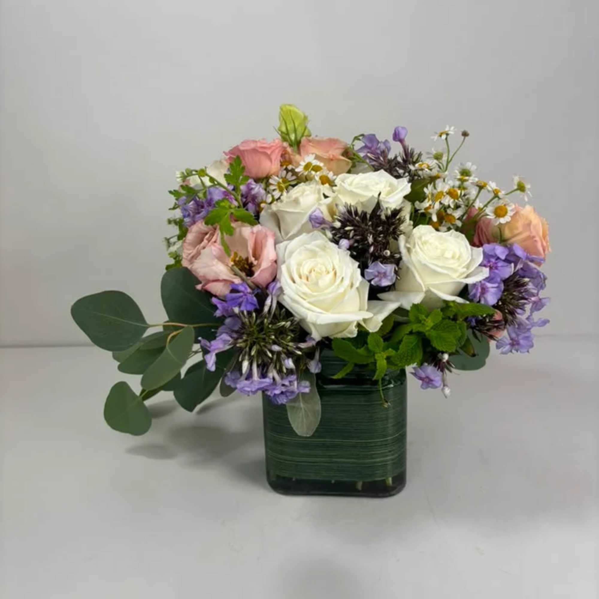 Mixed bouquet of white and pink roses with purple accents in a green vase