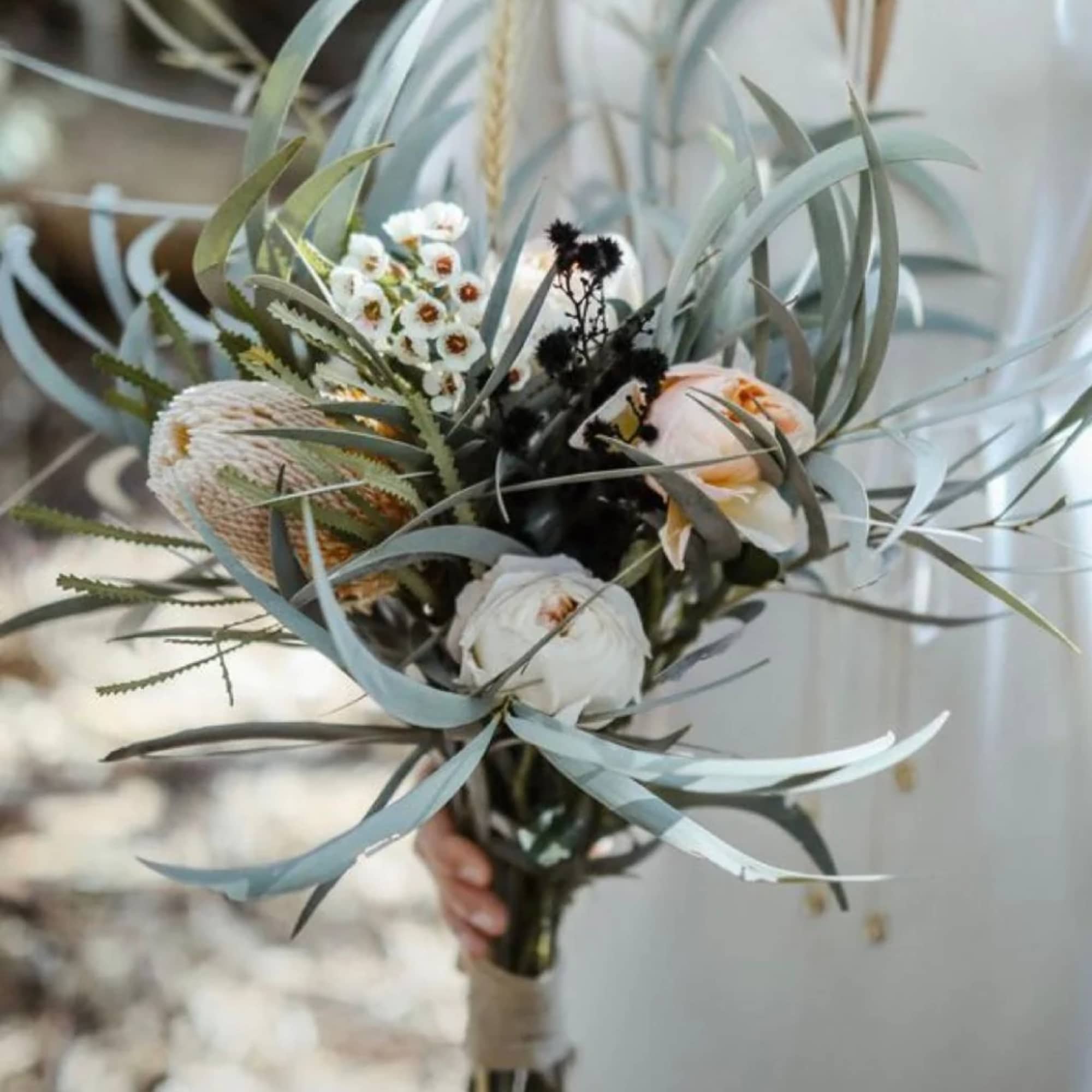 Handheld bouquet of white and peach flowers with long blue-gray foliage
