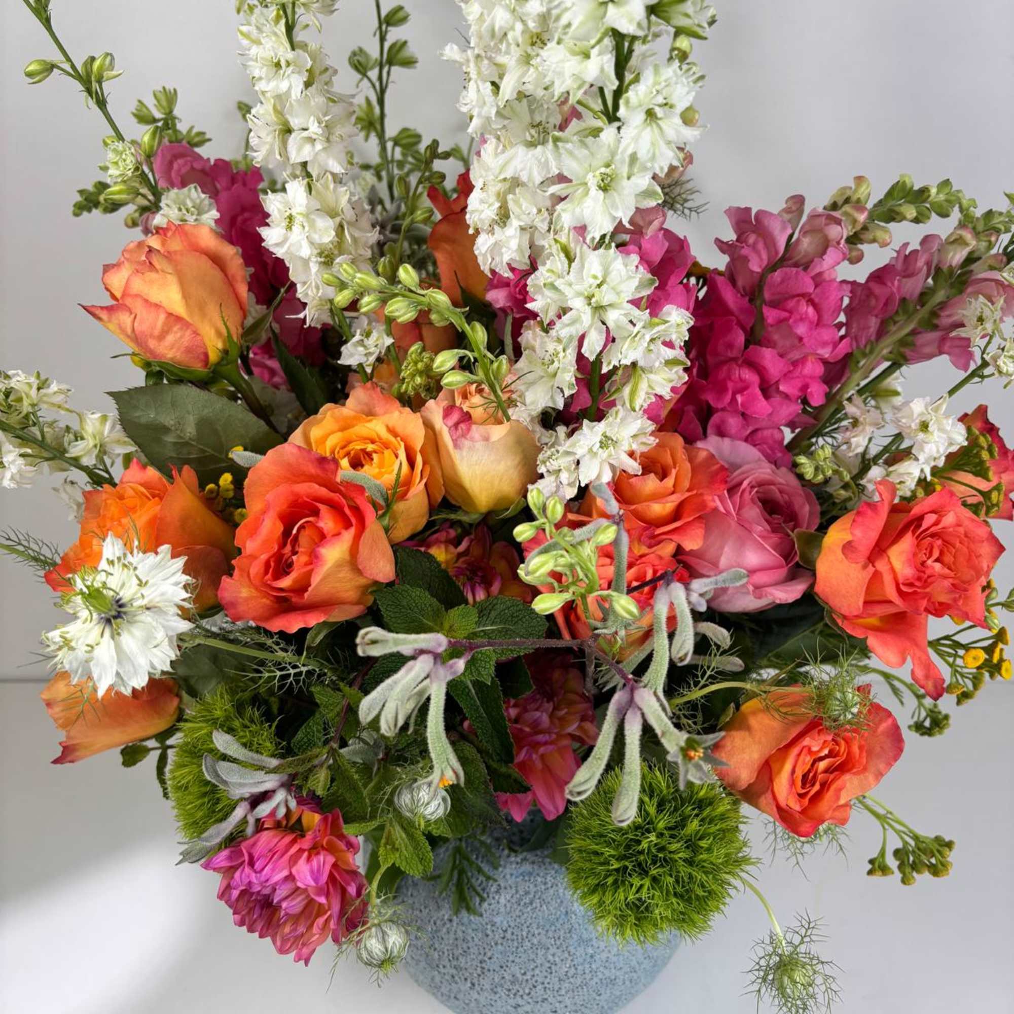 Mixed bouquet of orange and pink roses with white spikes in a blue vase
