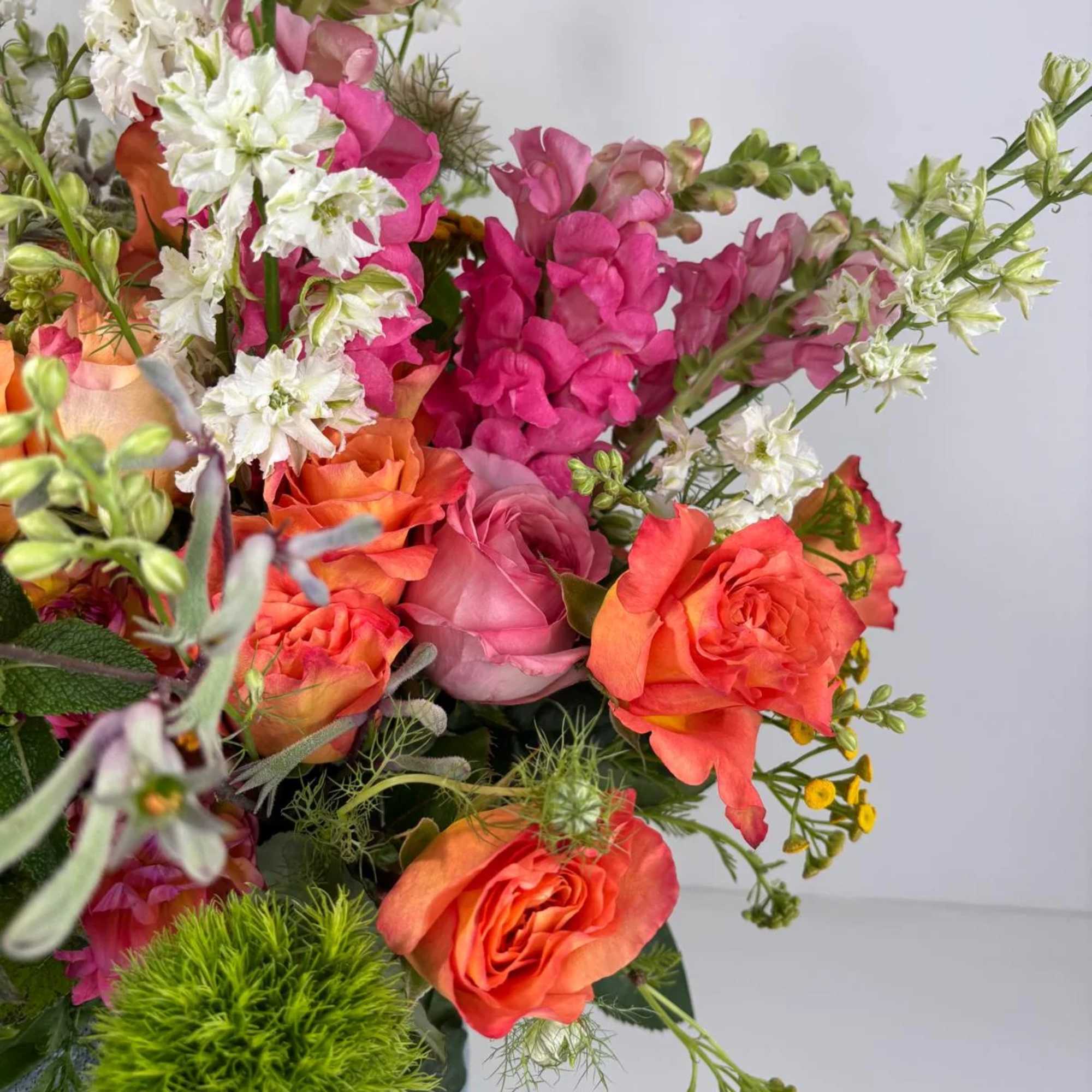 Bouquet of orange and pink roses with white and magenta snapdragons in a vase