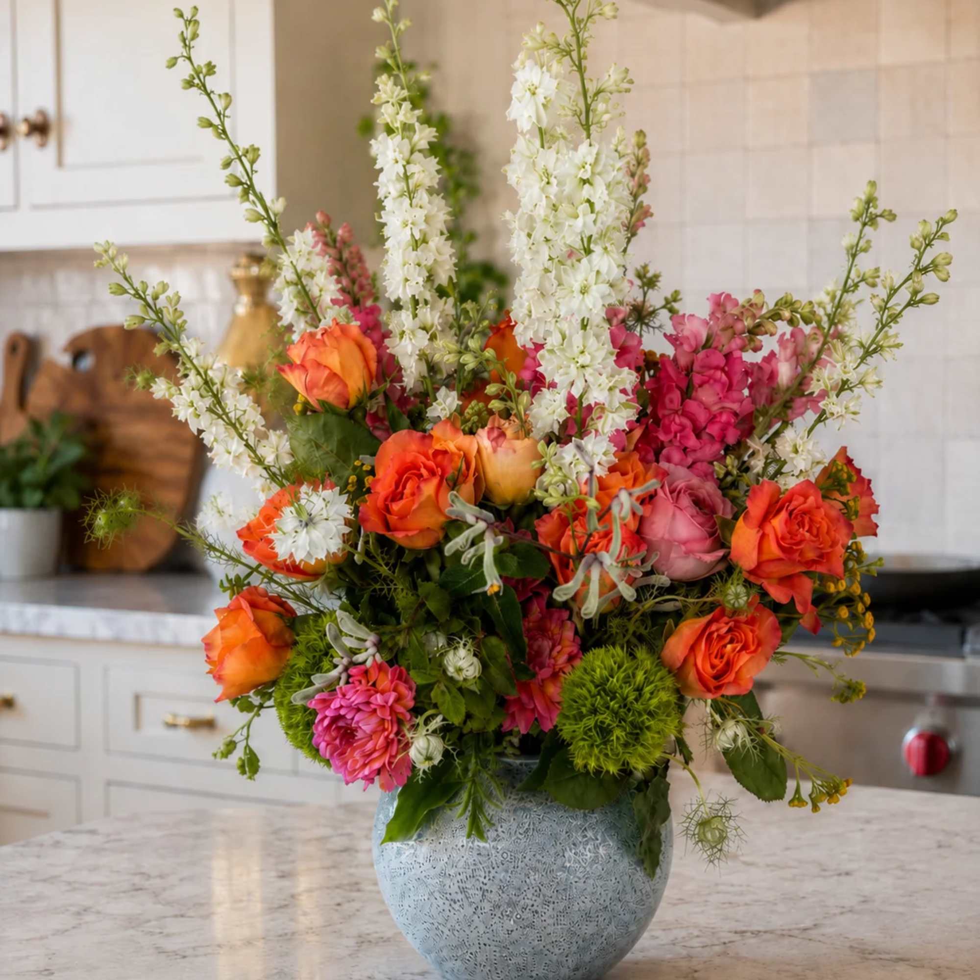 Colorful bouquet of orange roses, pink blooms, and white spikes in a blue vase
