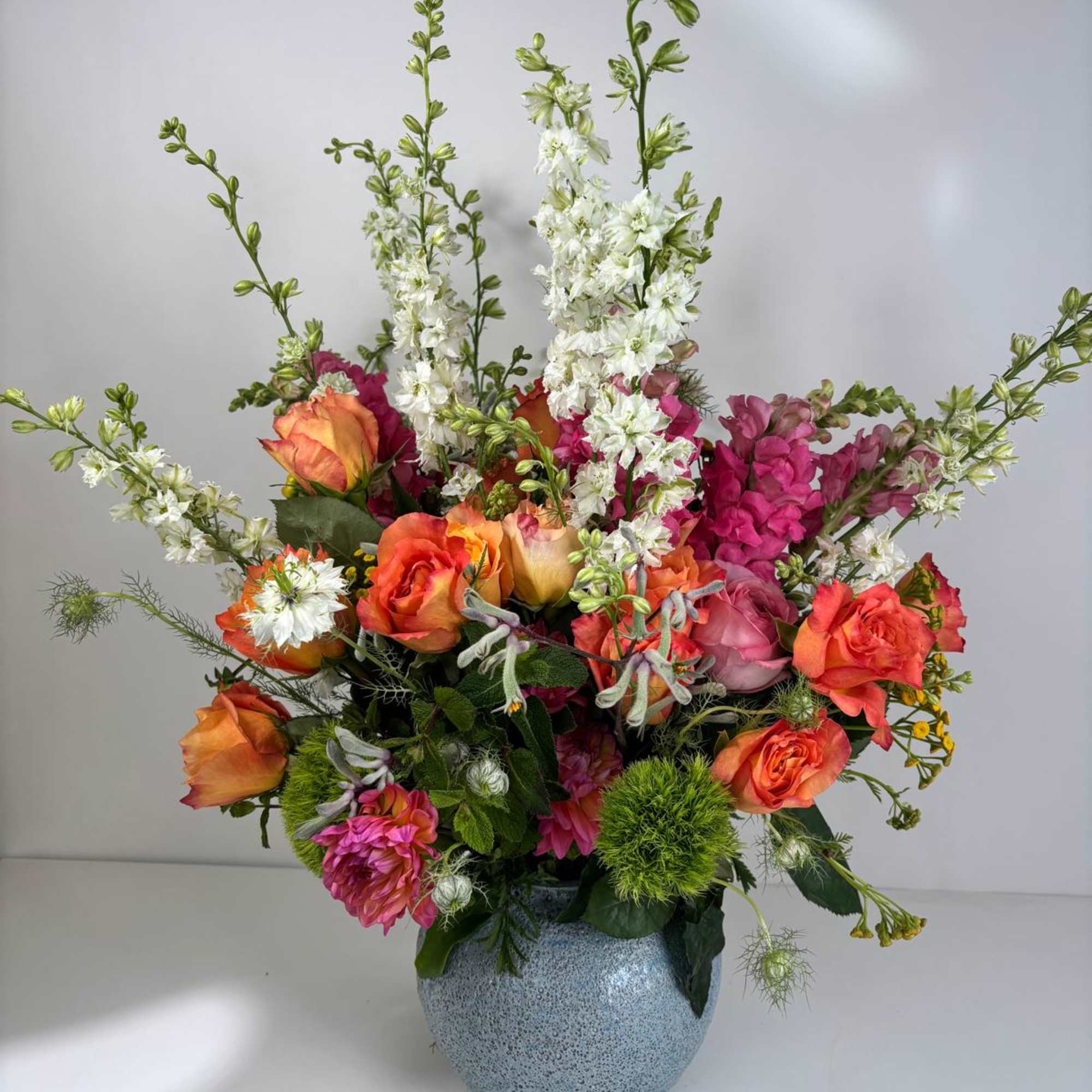 Colorful mixed flower arrangement in a blue vase with tall white spikes and orange roses