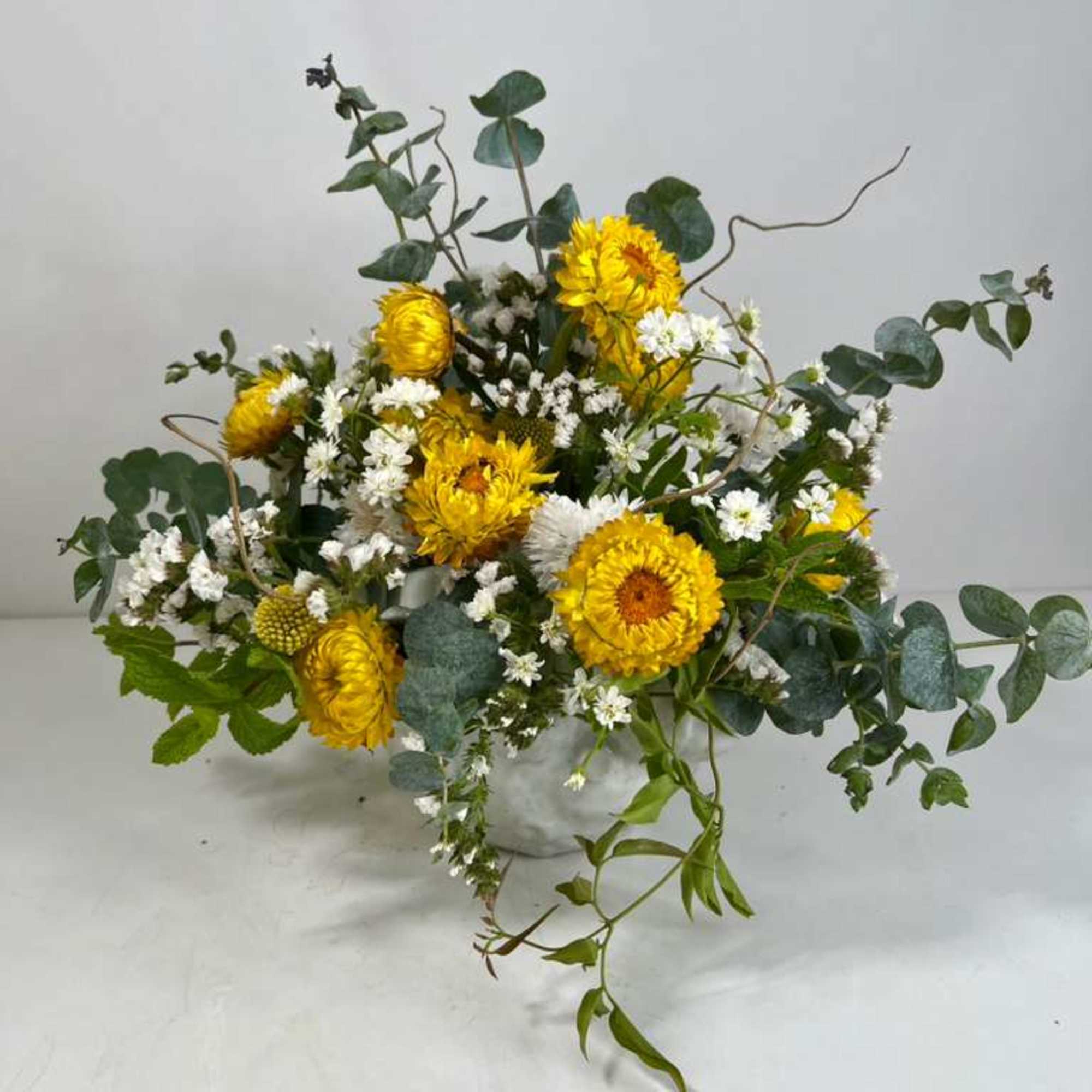 Yellow and white flowers in a low vase with trailing greenery