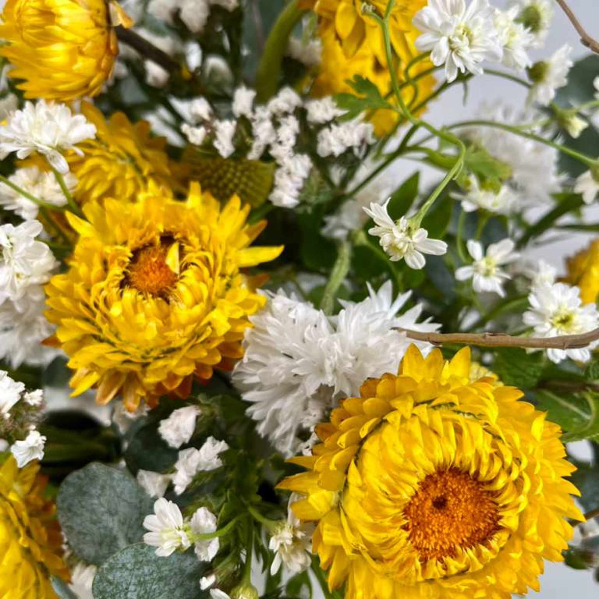 Bouquet of yellow blooms and small white flowers with eucalyptus accents